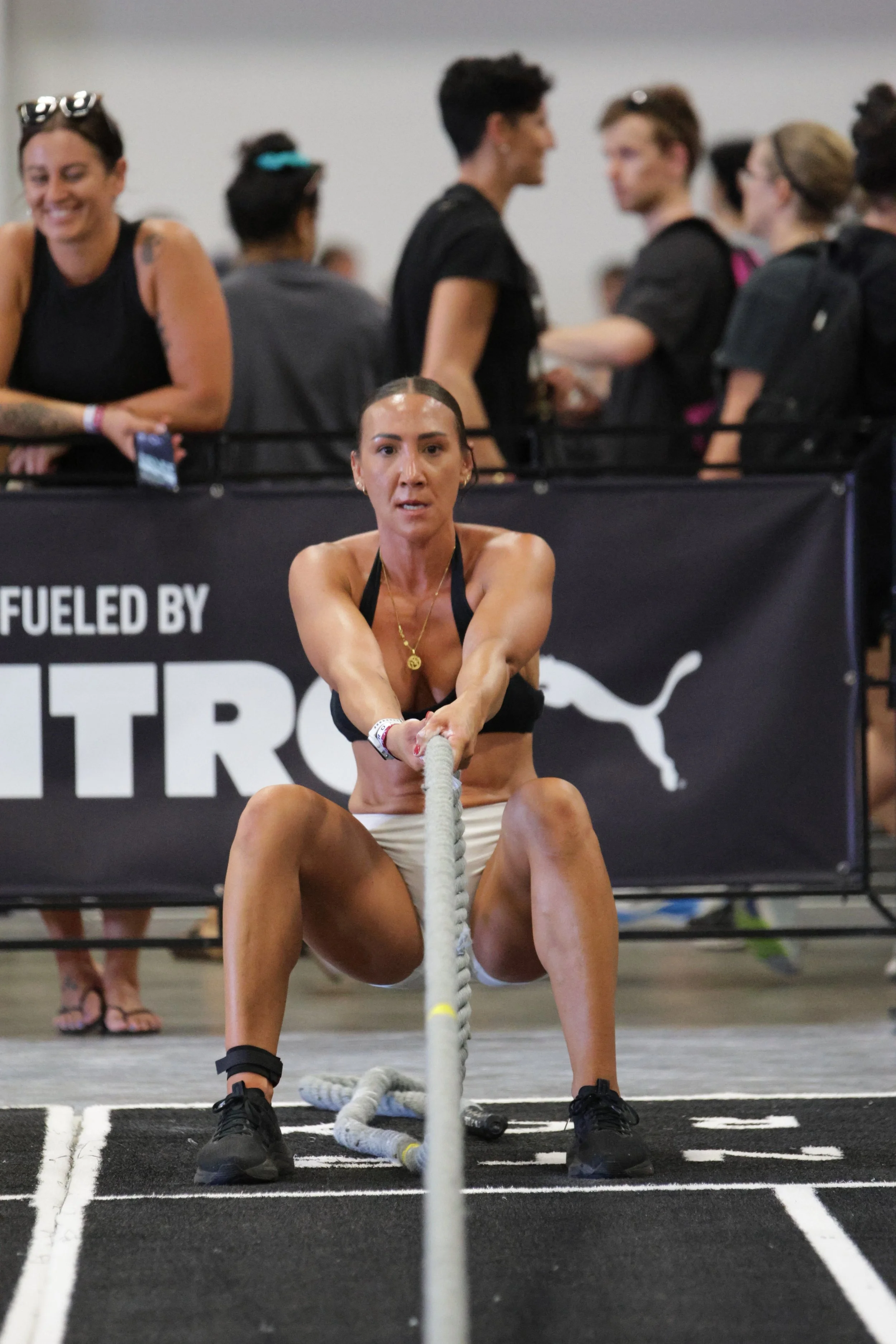 Woman pulling a rope during a fitness competition in an indoor gym with an audience in the background.