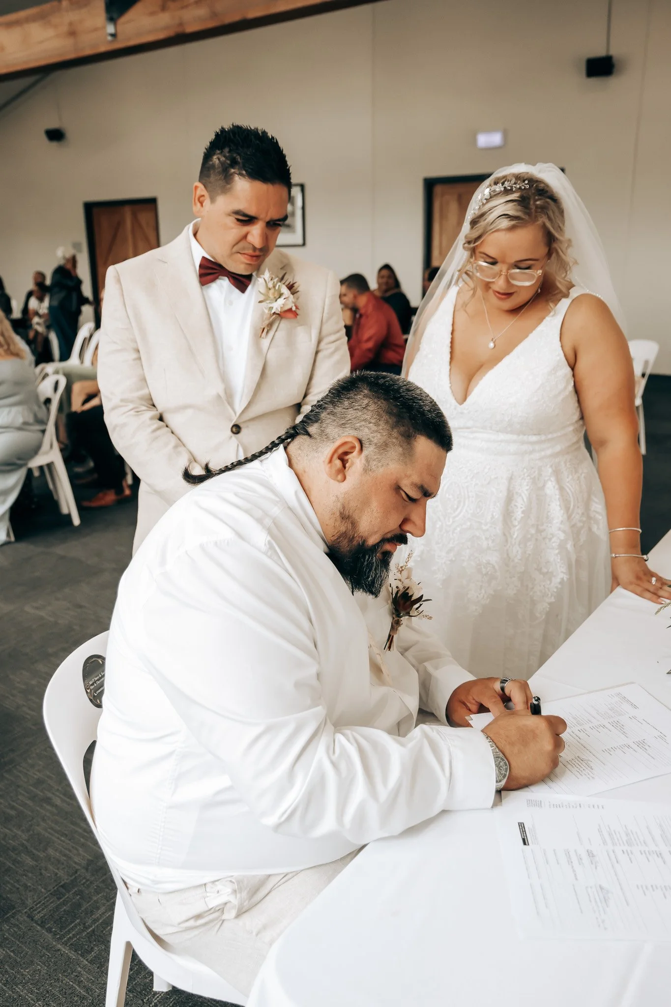 A couple signs a marriage license at a wedding ceremony with guests in the background.
