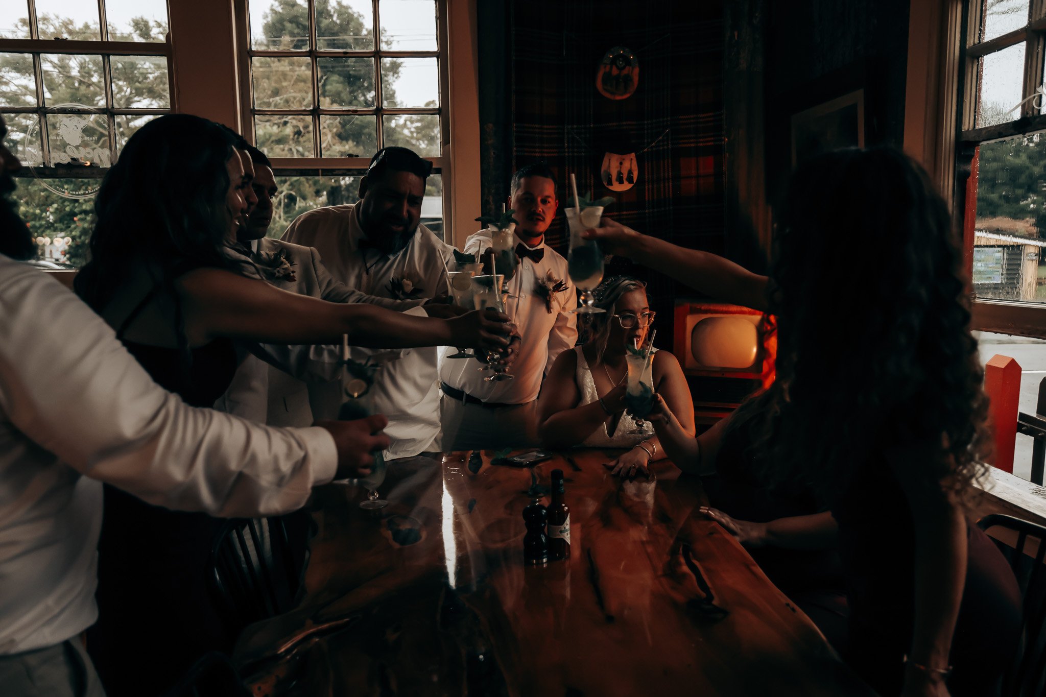 A group of people dressed in formal attire, celebrating with drinks inside a restaurant or bar with large windows and natural light.
