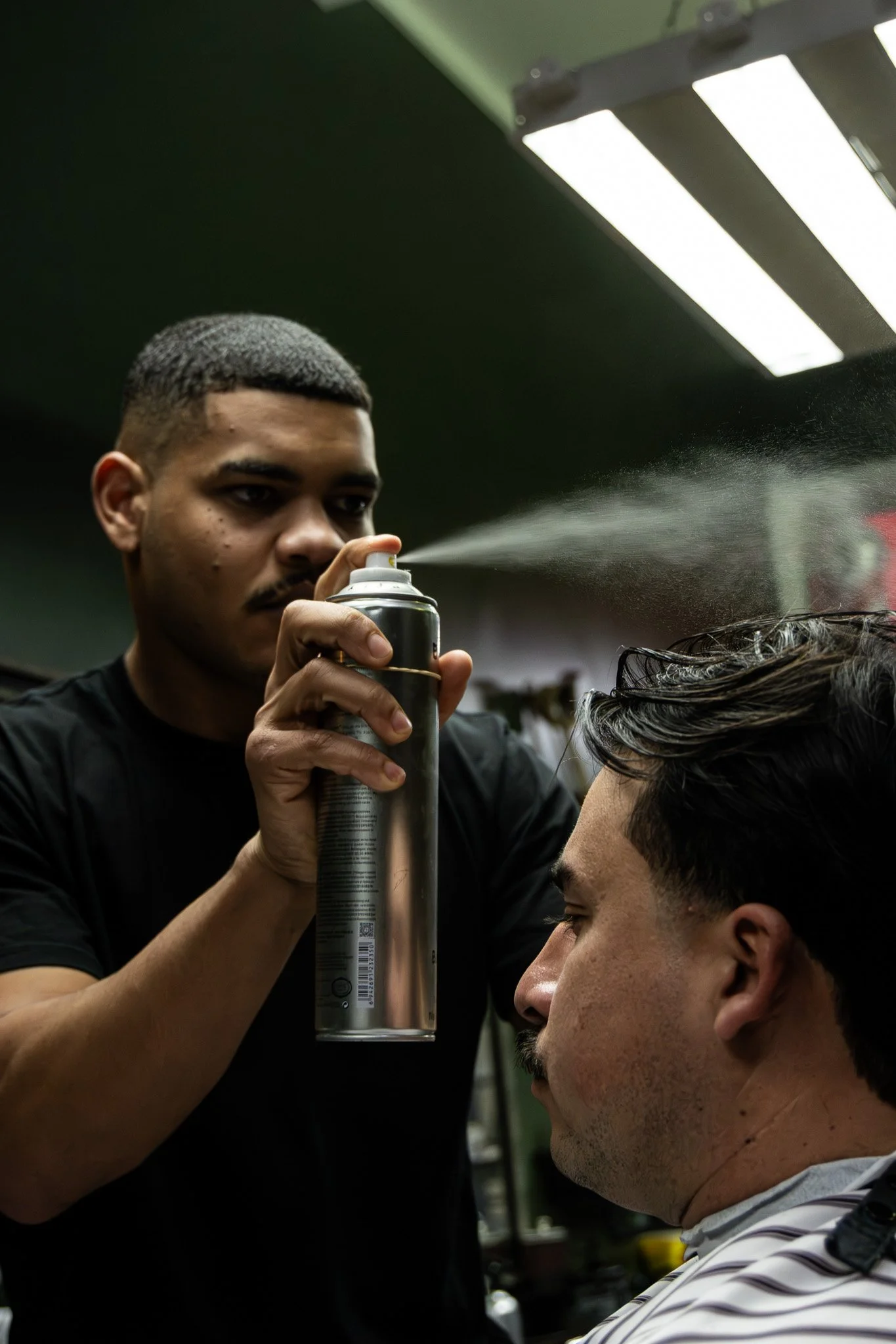 Barber using hair spray on a customer’s hair in a barbershop.