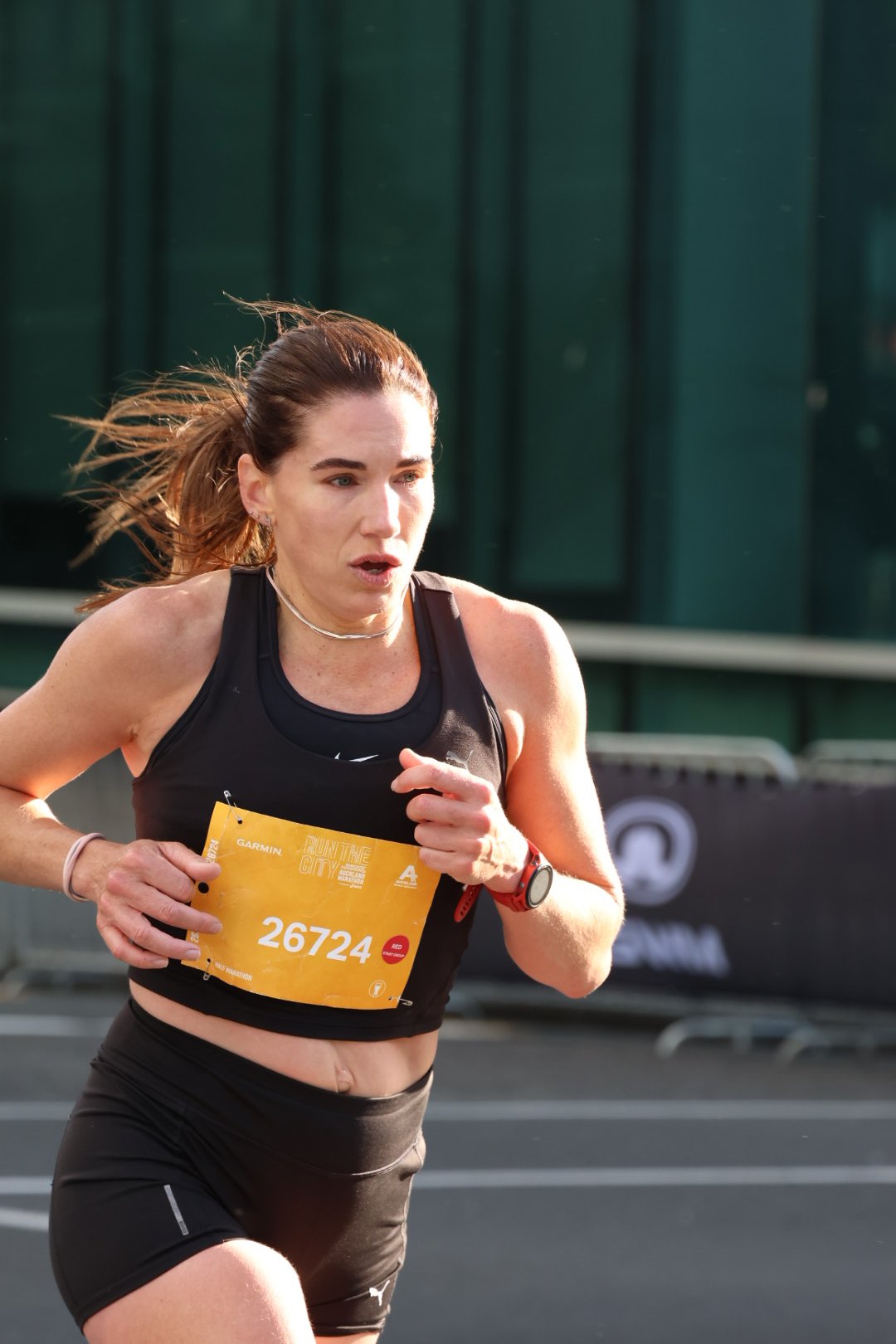 A woman running in a marathon, wearing a black sports outfit, a red watch, and a yellow race bib with the number 26724.