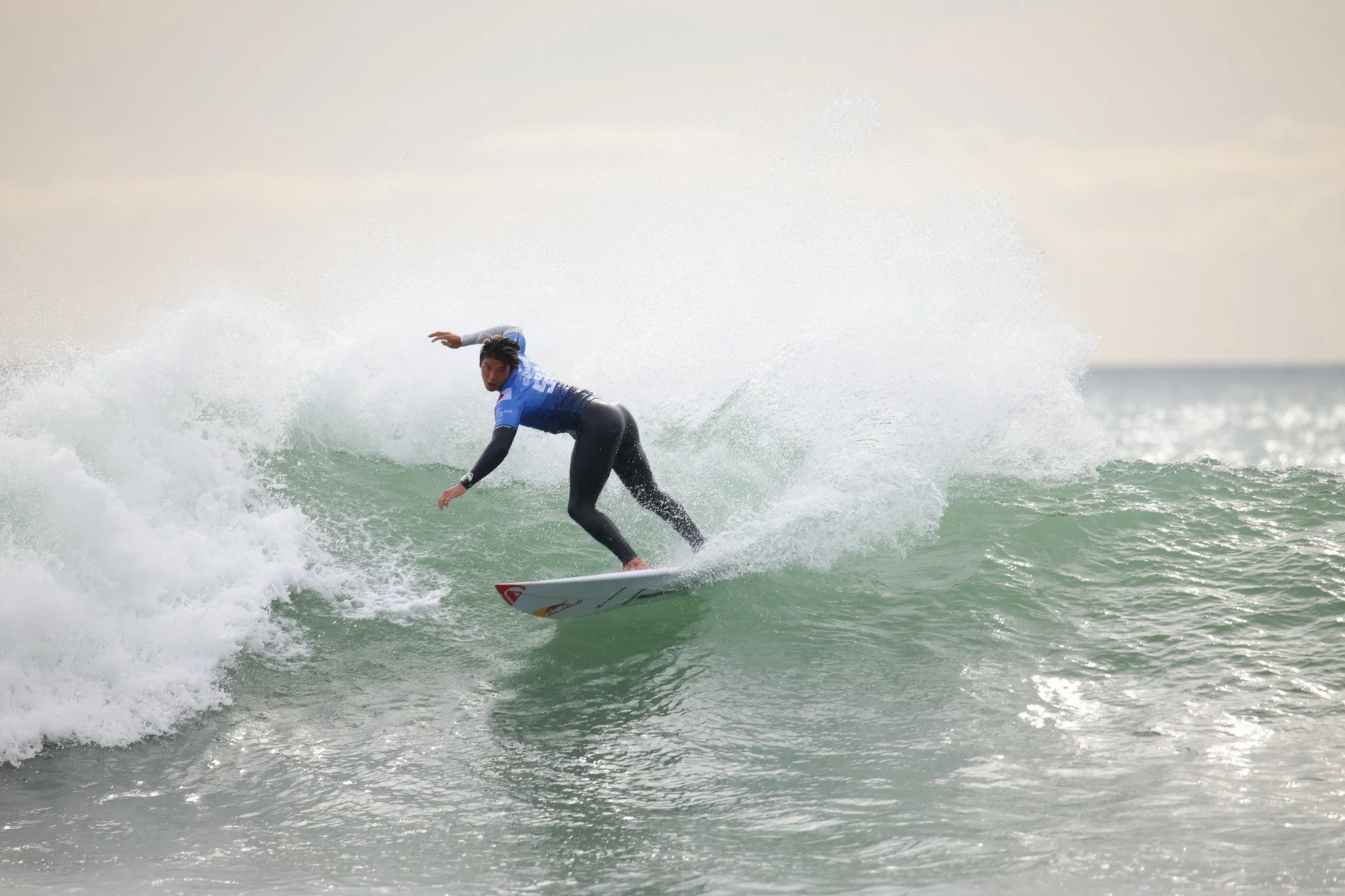A person surfing on a wave in the ocean, wearing a blue and black wetsuit.