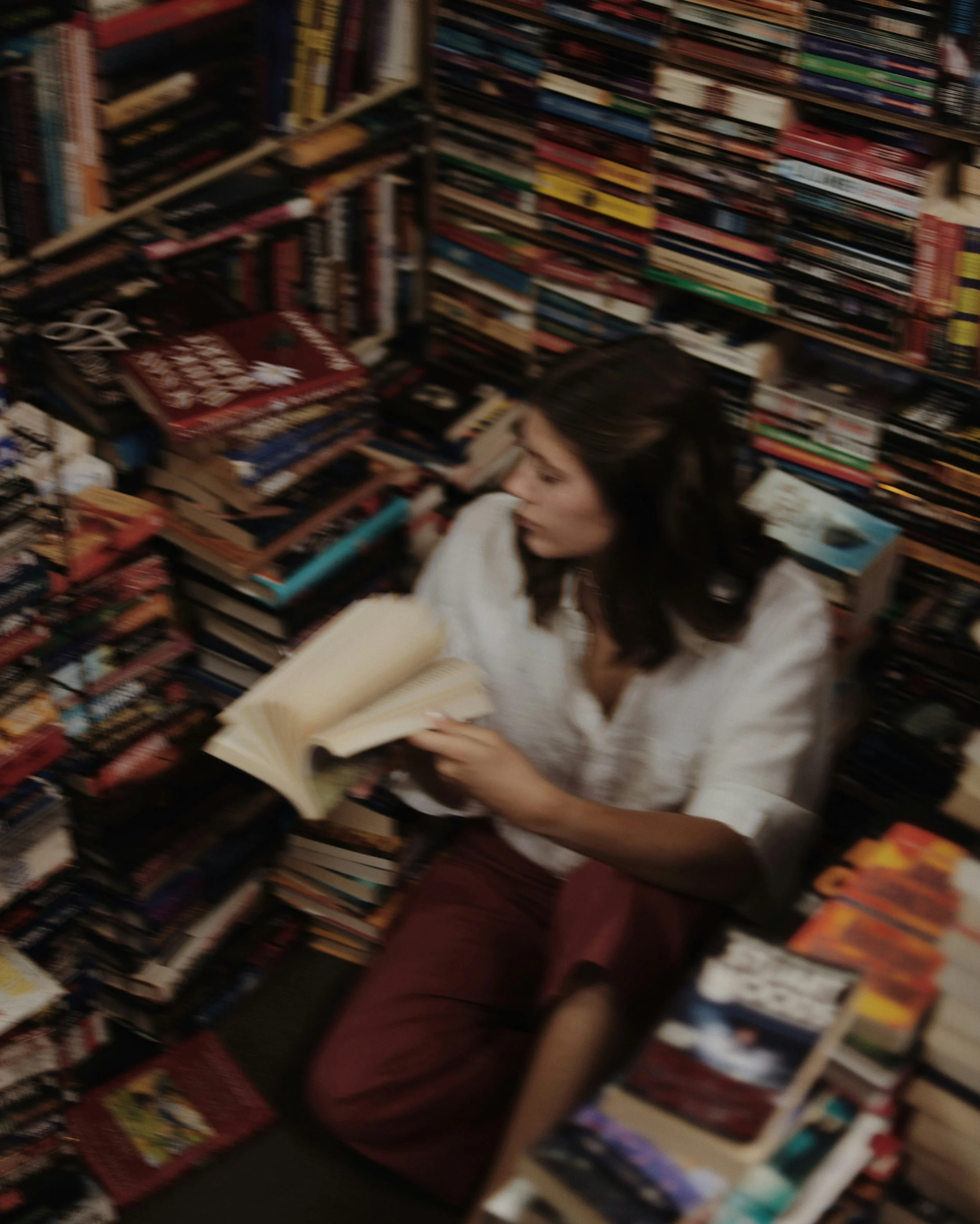 Persona leyendo un libro en una librería repleta de estantes con muchos libros.