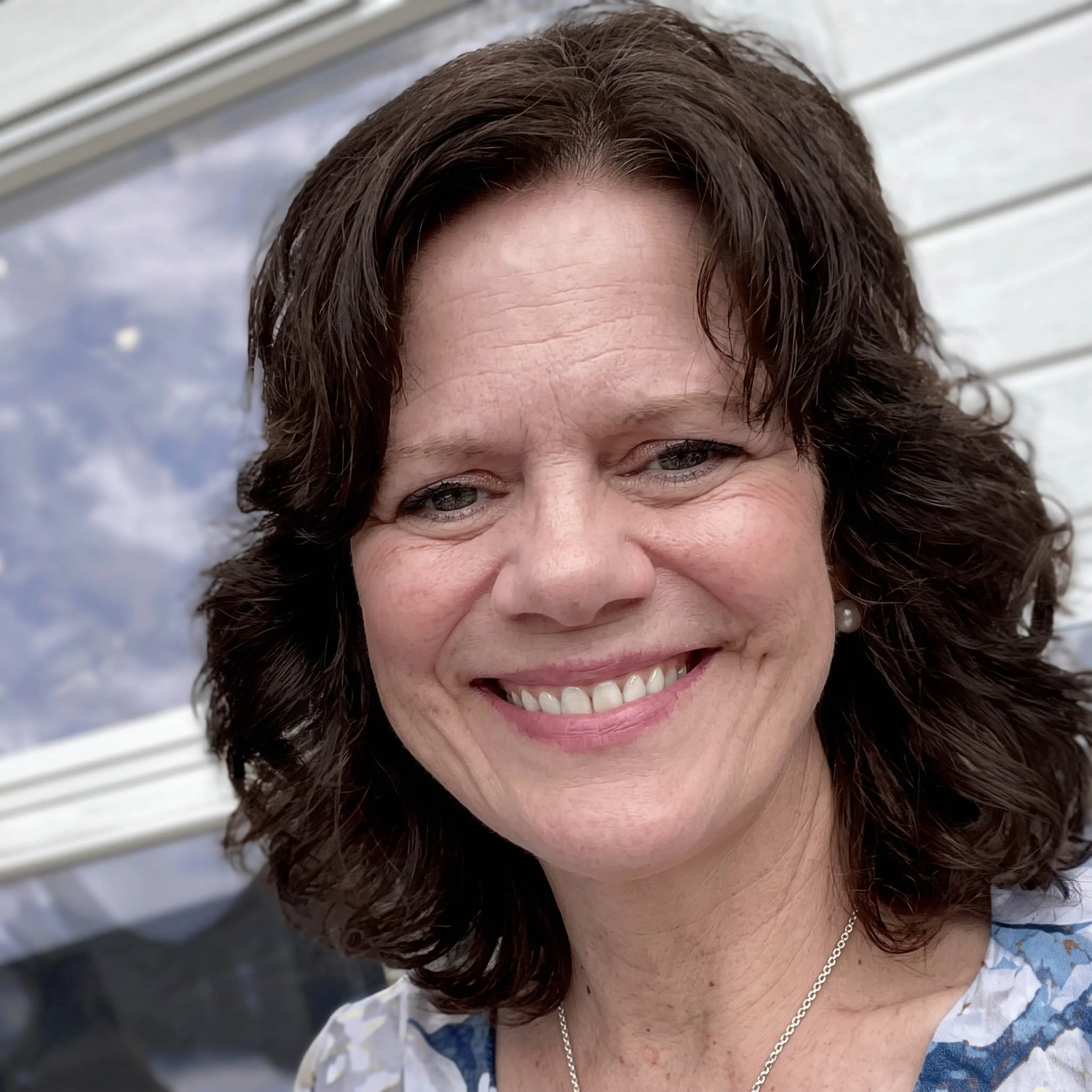 Lyn kvinne med brunt, bølget hår smiler. Bakgrunn av hvite vegger og vannpiper.