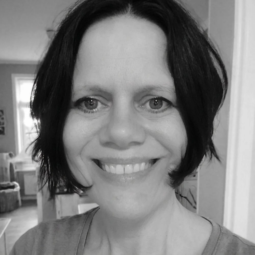 Et svart-hvitt bilde av en smilende kvinne med kort svart hår, tatt innendørs.