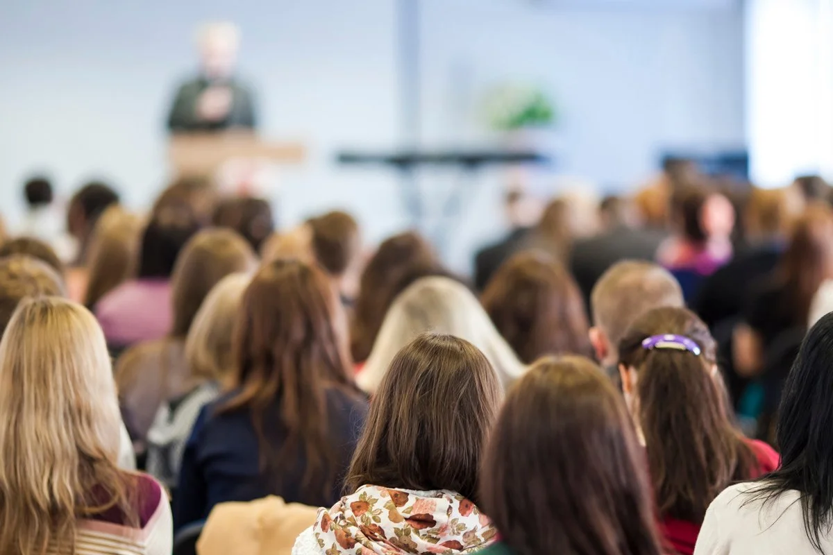 A speaker giving a presentation to a large audience in a conference room.