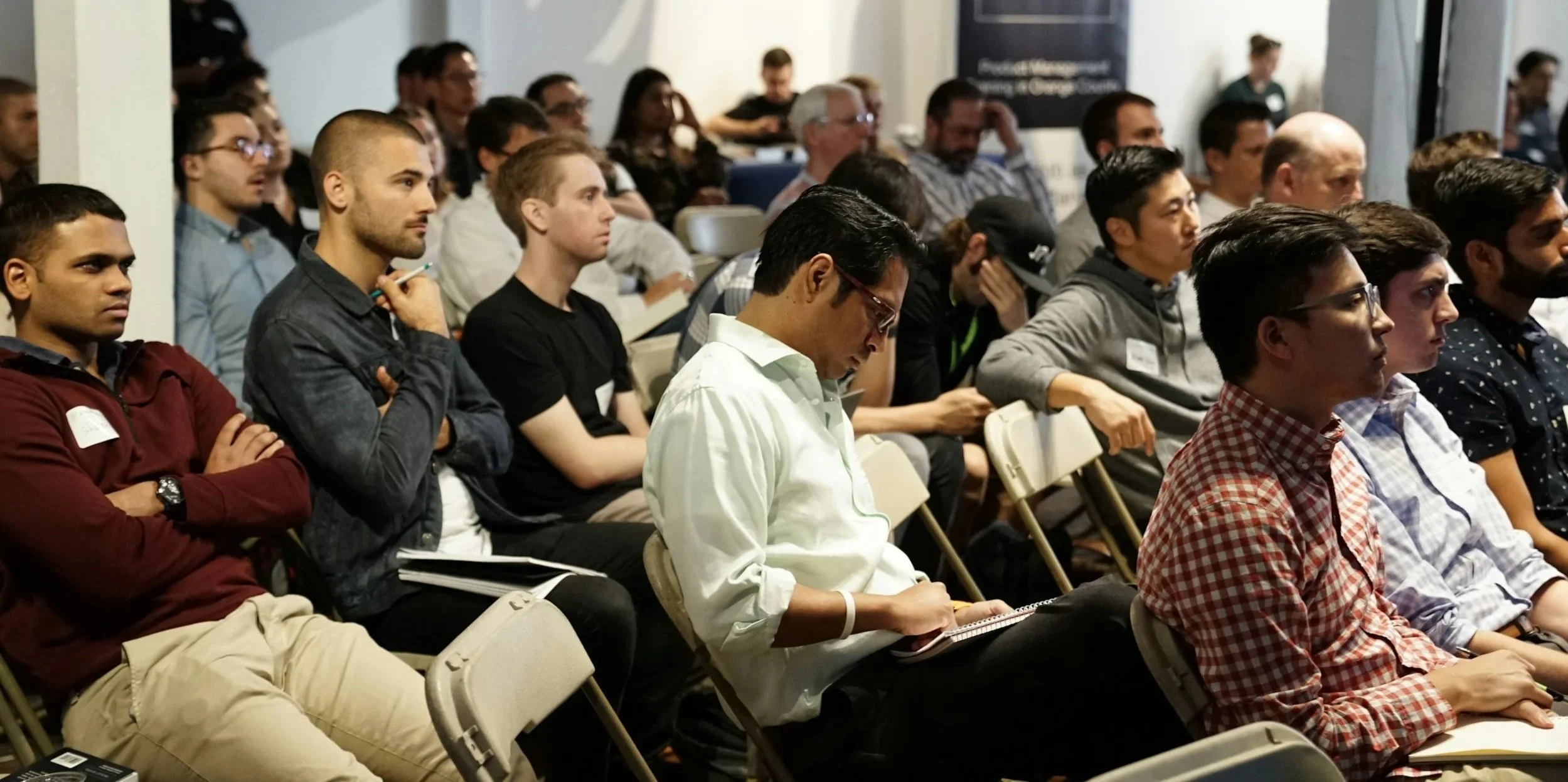 Audience attending a conference or seminar, seated and attentively listening to a speaker.
