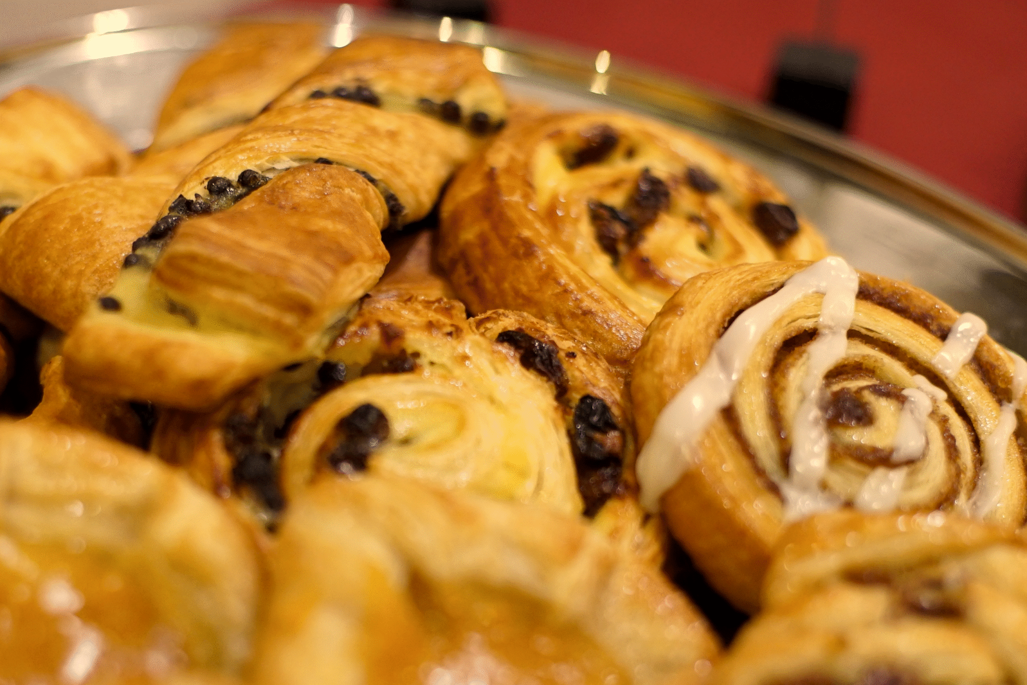 Close-up of cinnamon rolls with chocolate chips and icing on a tray.