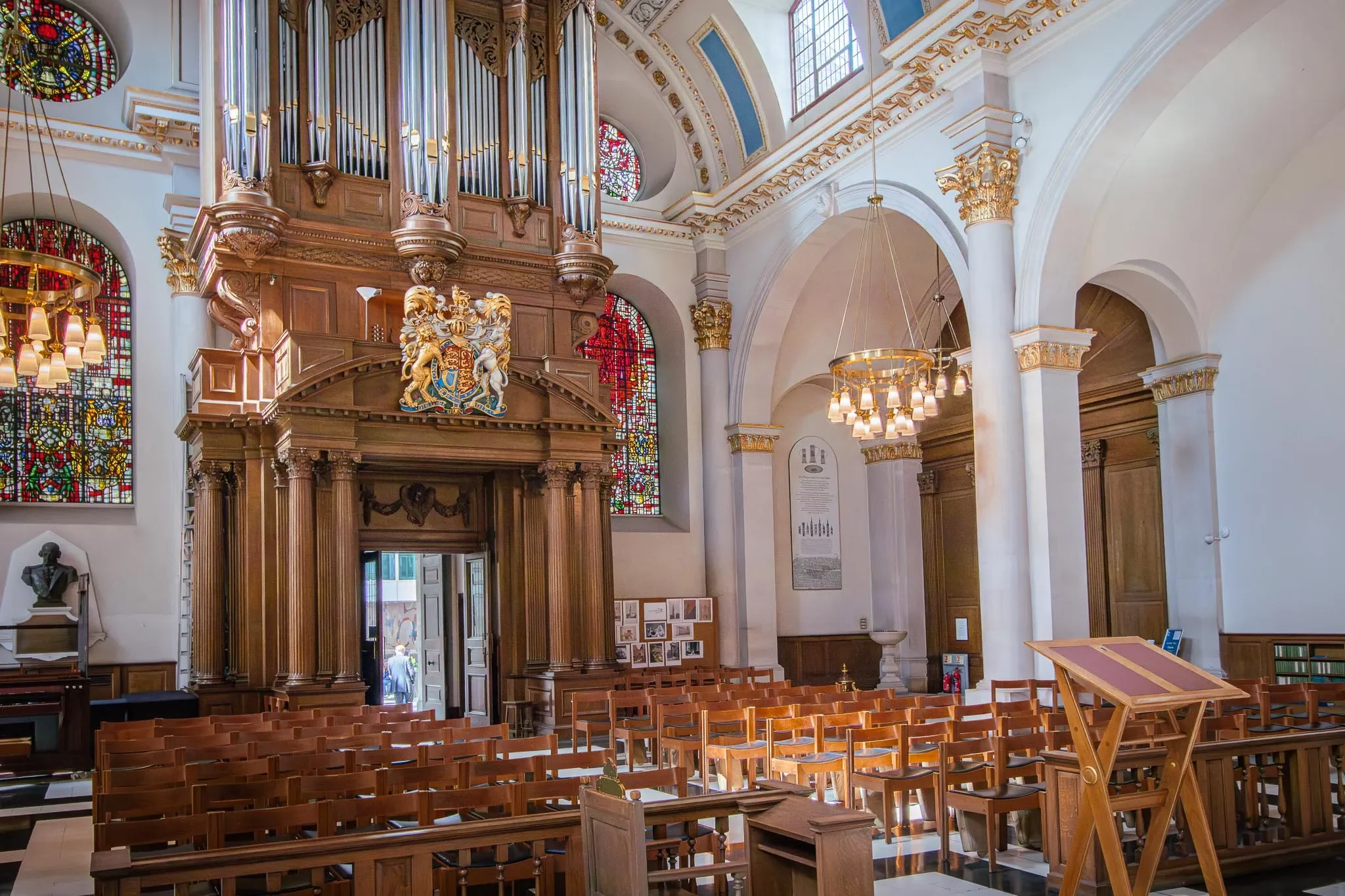 Interior of a church with wooden pews, stained glass windows, a pipe organ, and decorative gold accents.