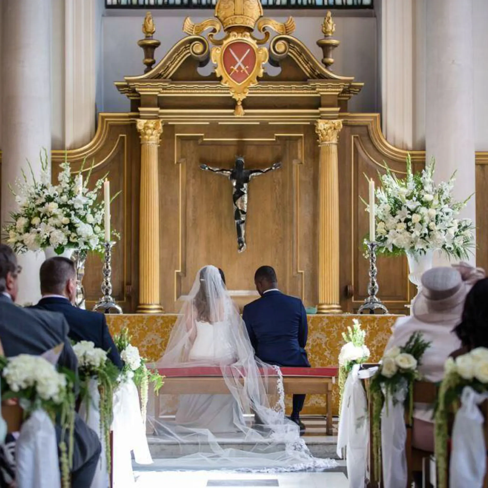 A church altar with a crucifix, floral arrangements, and an ornate wooden backdrop