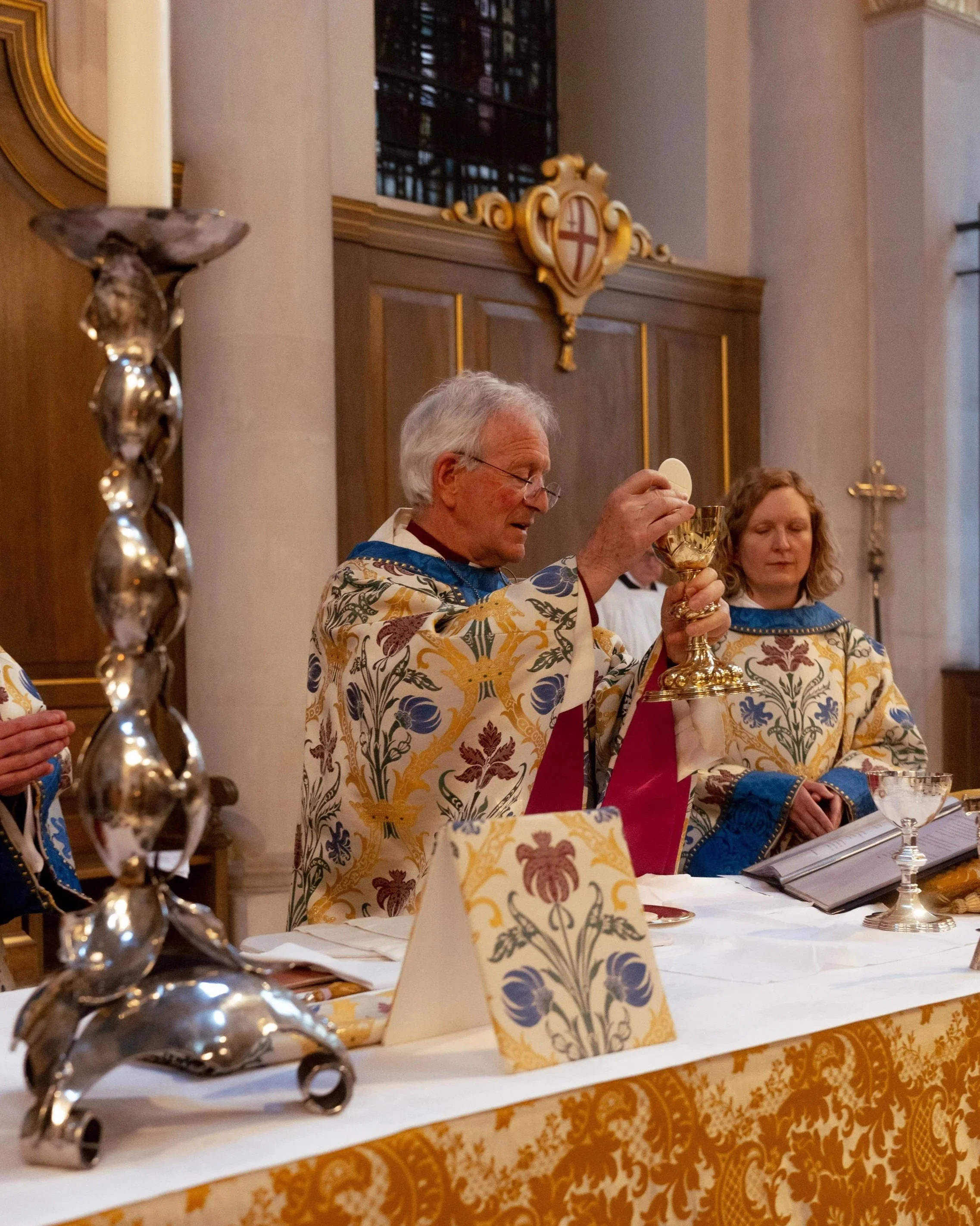 Priest and woman celebrating communion during a religious ceremony in a church, with religious symbols and ornate decorations in the background.