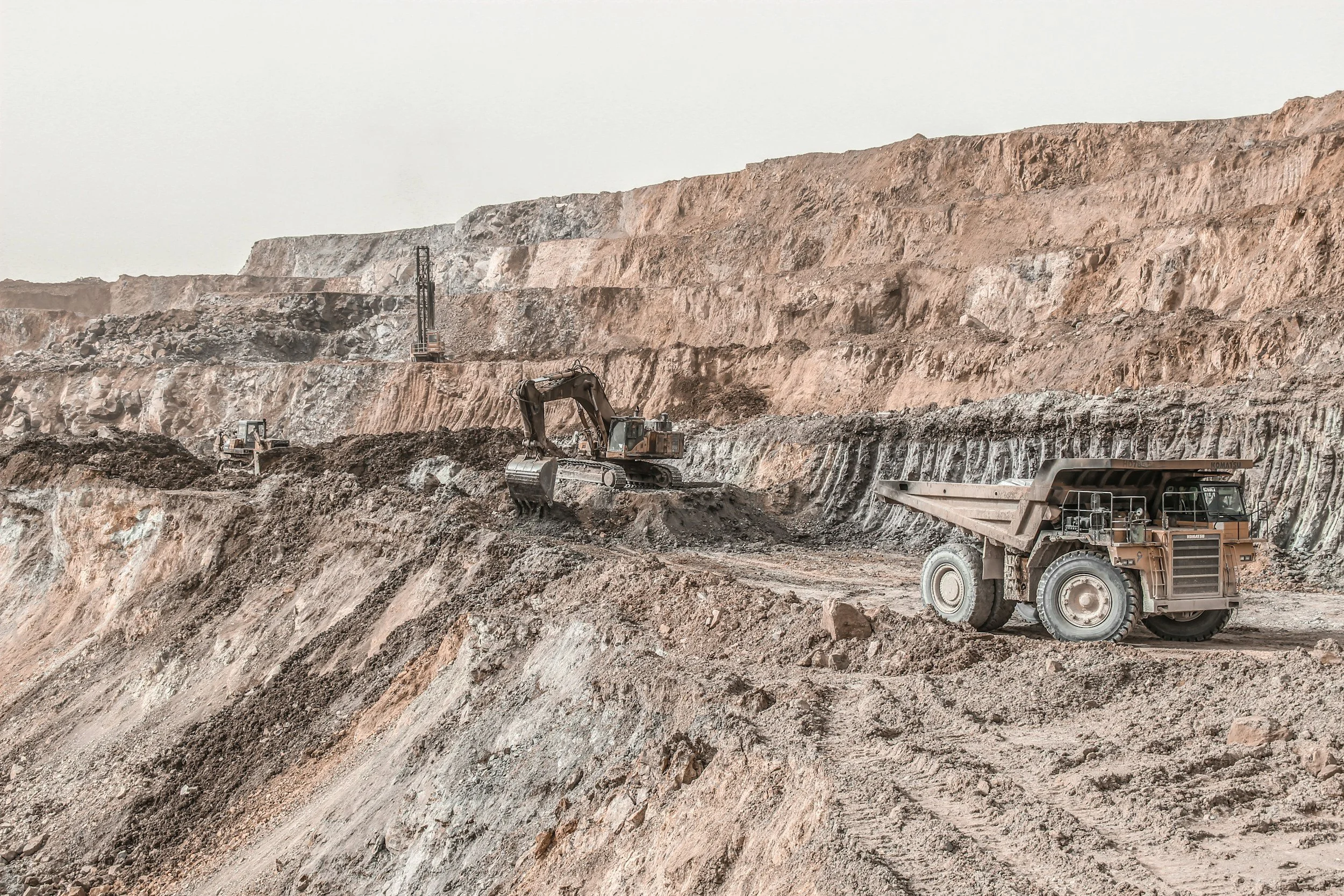Earth-moving construction site with excavators and a dump truck working on a large dirt and rock excavation.