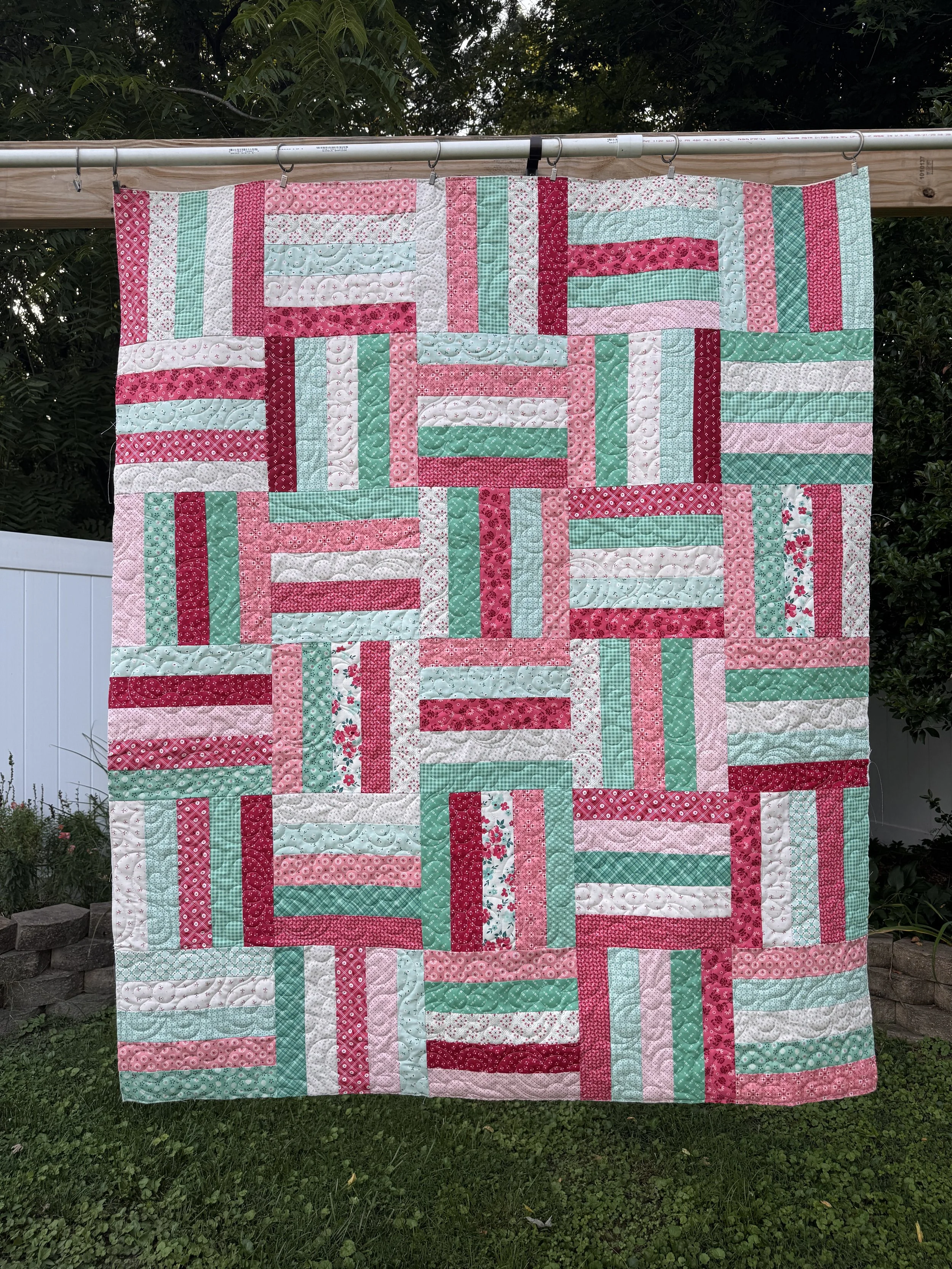 Colorful quilt hanging outdoors with trees in the background.