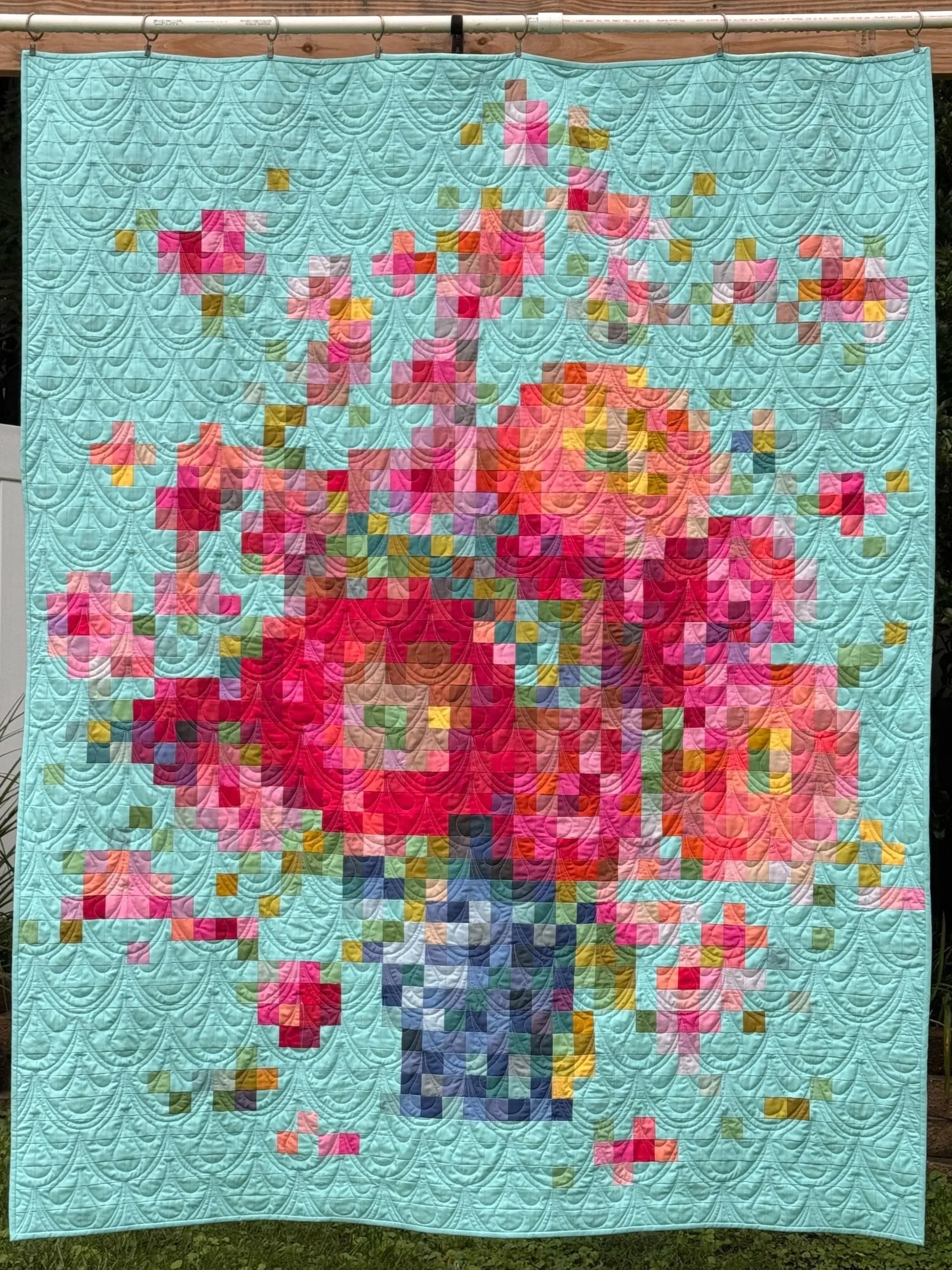 A colorful quilt featuring a pixelated image of a person in a pink top and orange pants, standing against a light blue background with a pattern of stitched arcs.