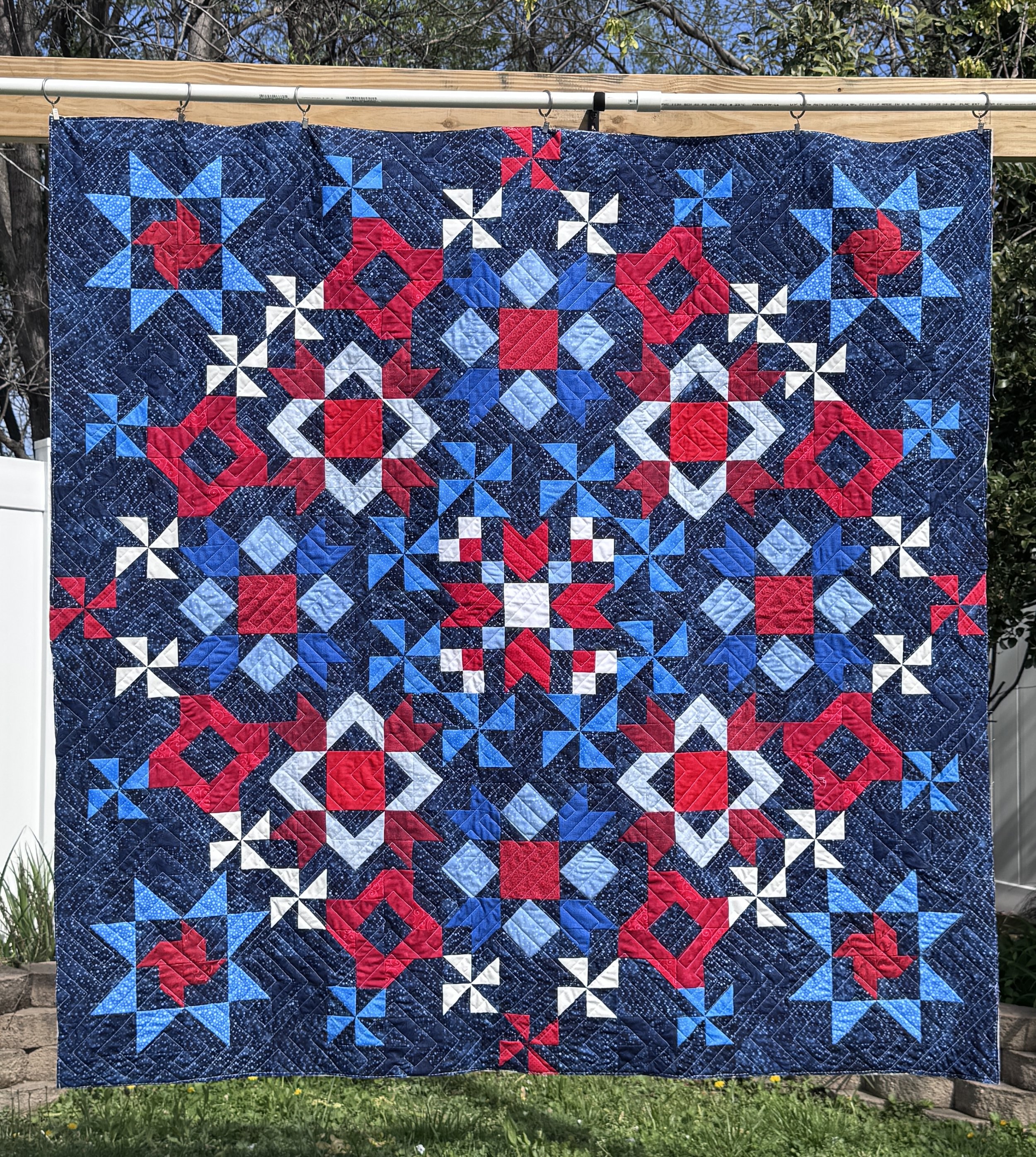 A colorful quilt with a patriotic design of red, white, and blue patterns, hanging outdoors on a clothesline.