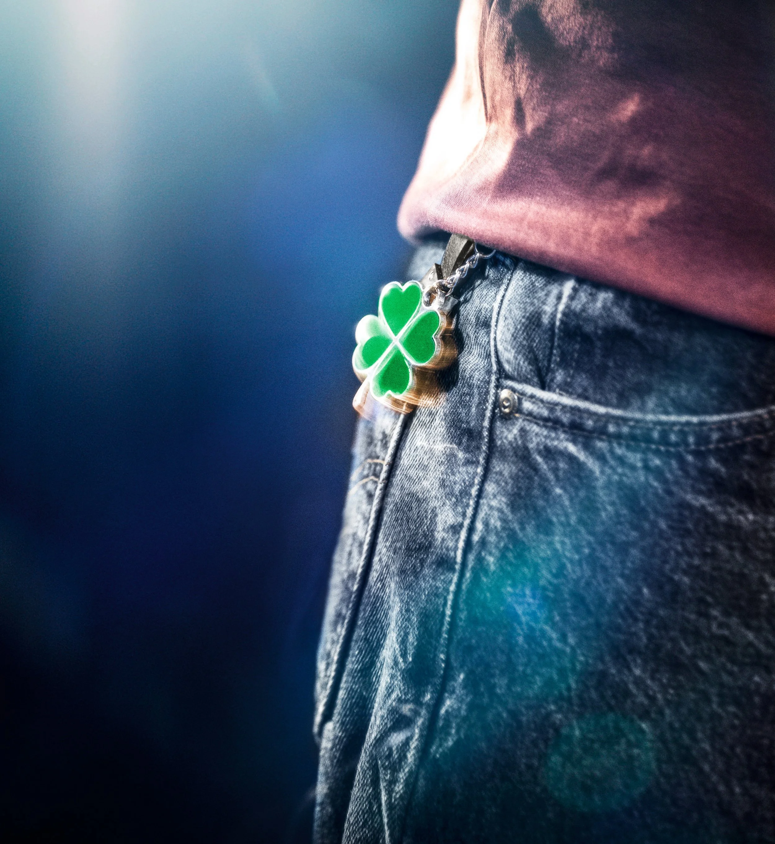 Close-up of a person wearing denim jeans and a maroon shirt, with a shamrock-shaped keychain hanging from the pocket. Good luck charm. Ad photo.
