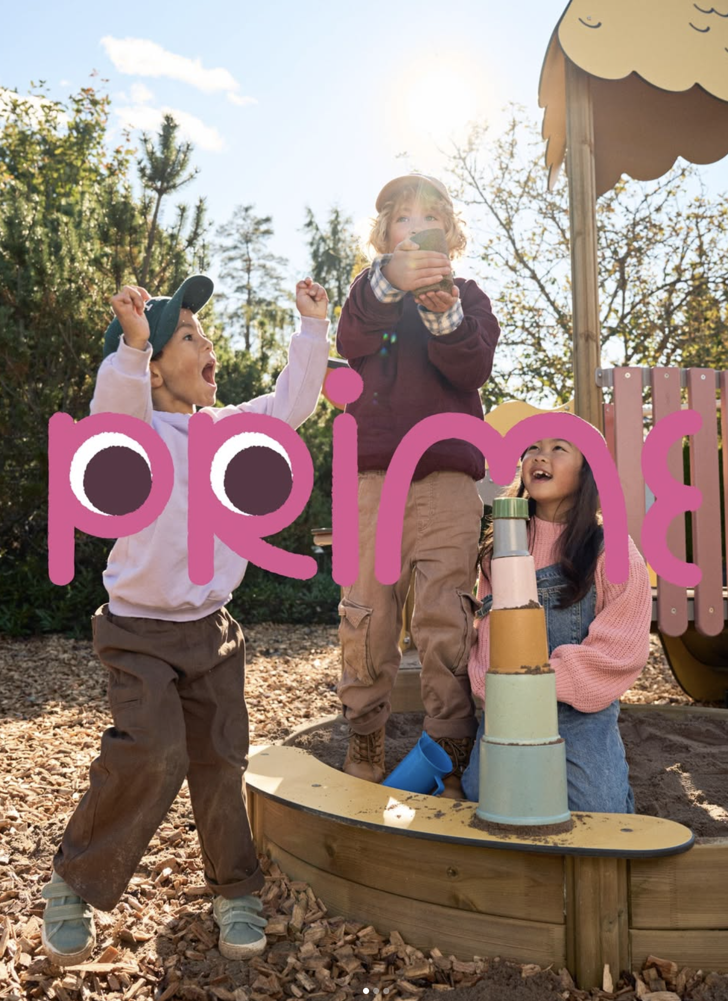 Children playing in a sandbox at a playground during daytime, with a slide in the background and trees around. Ad photo.