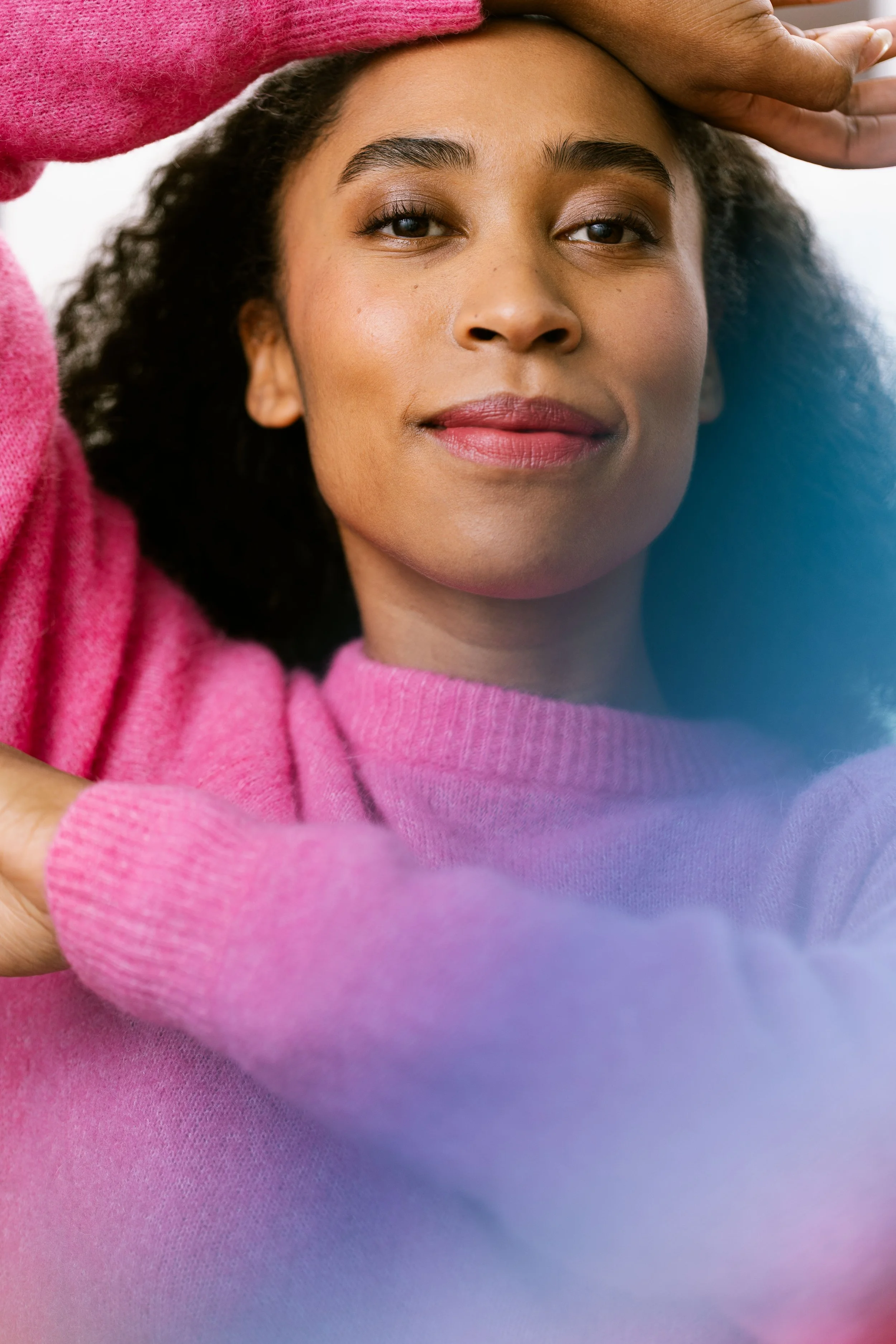 A woman with dark curly hair wearing a pink sweater, looking softly at the camera. Brand photography for banking.