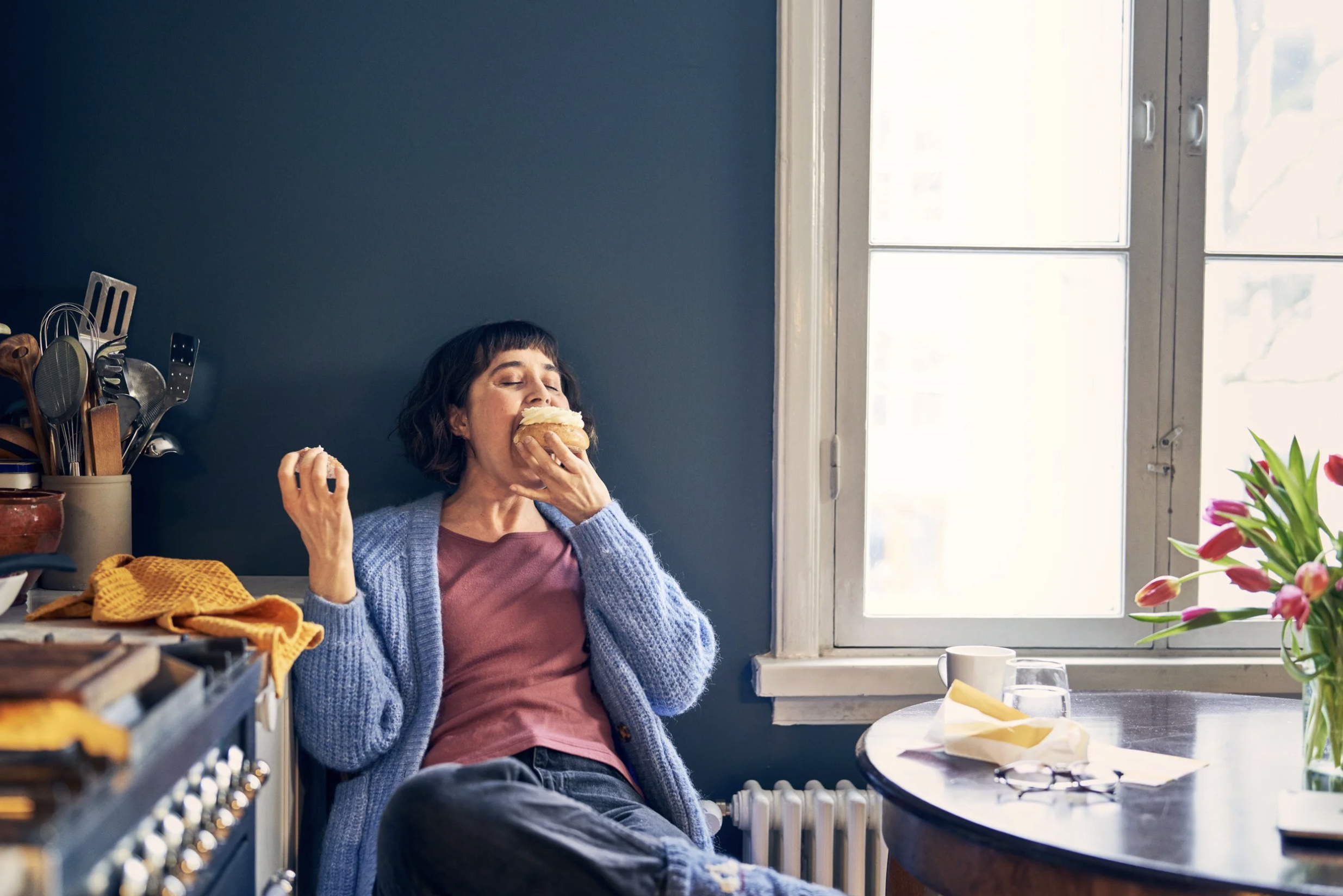 A woman with short dark hair biting into a pastry. Brand photo for a supermarket.
