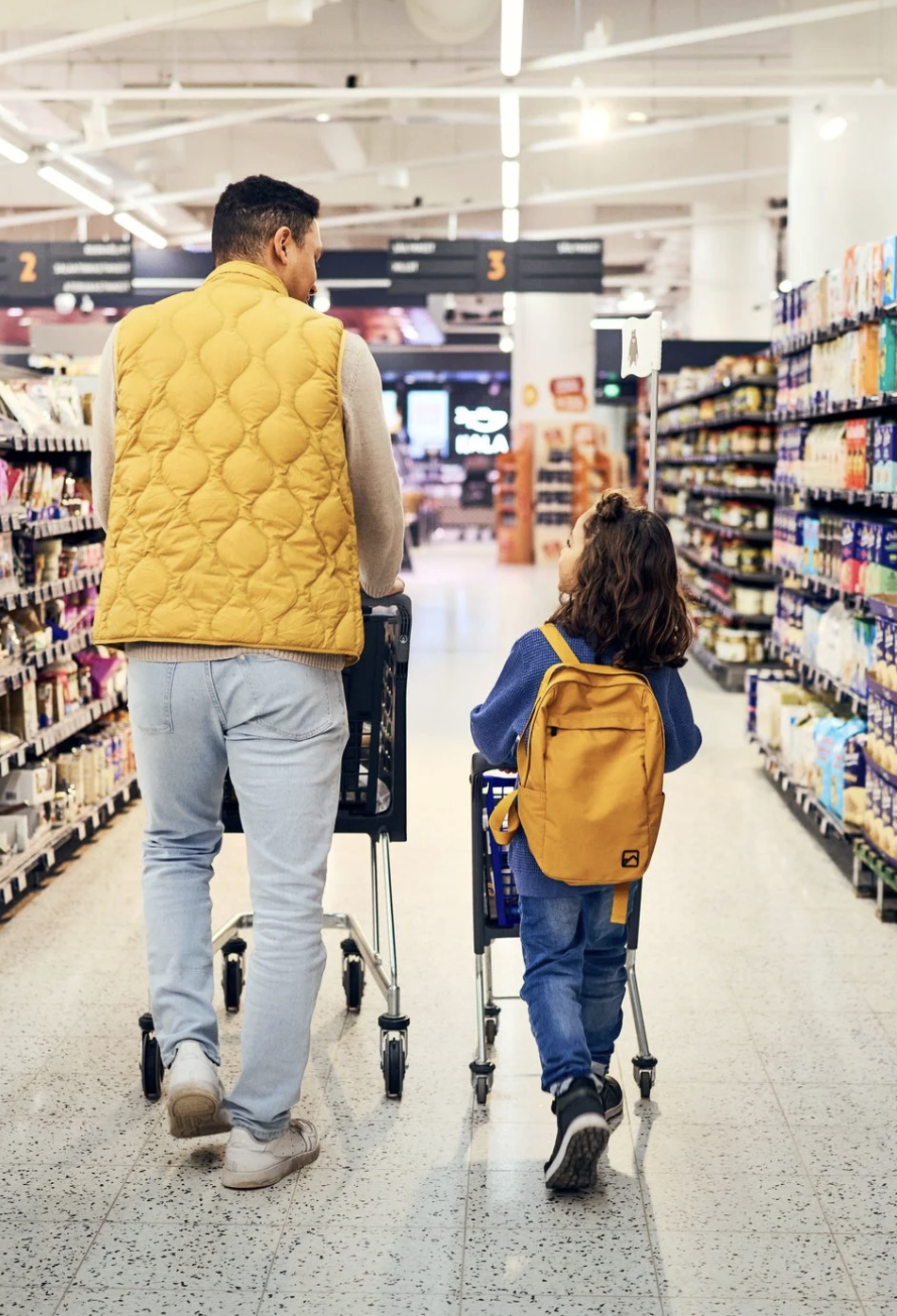 An adult and a child with roller carts shopping in a grocery store aisle. Brand photography for a supermarket.