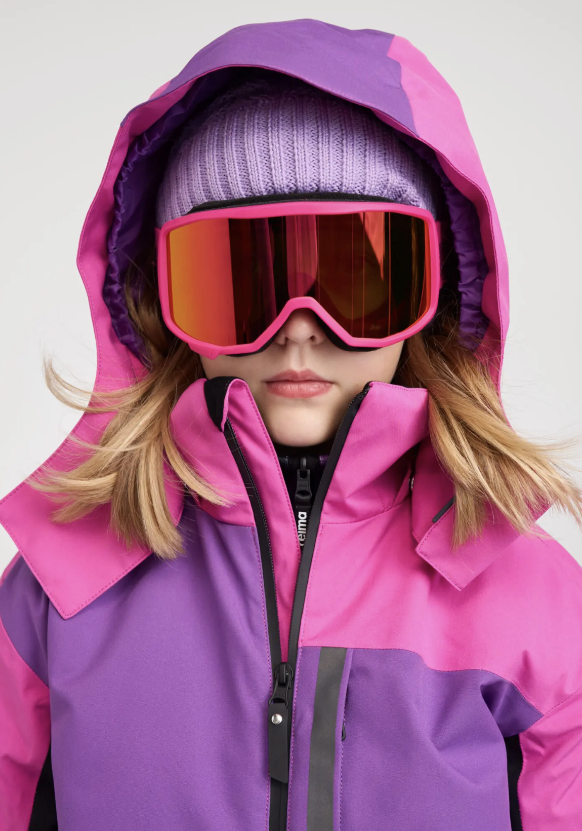 A girl dressed in bright pink and purple winter ski gear. Ad photo for Reima.