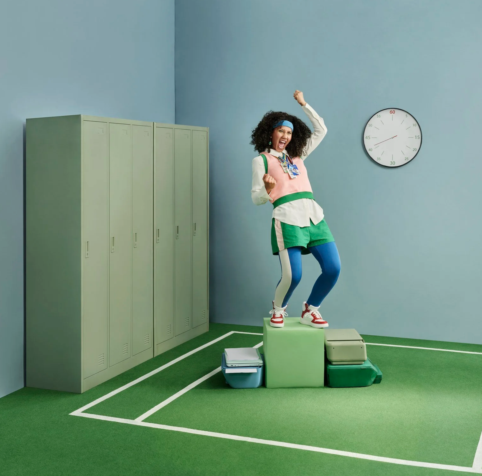 A woman with curly hair, wearing colorful athletic clothing, stands on a green pedestal with her arms raised in triumph inside a colorful gym or sports facility.  Advertising photography.