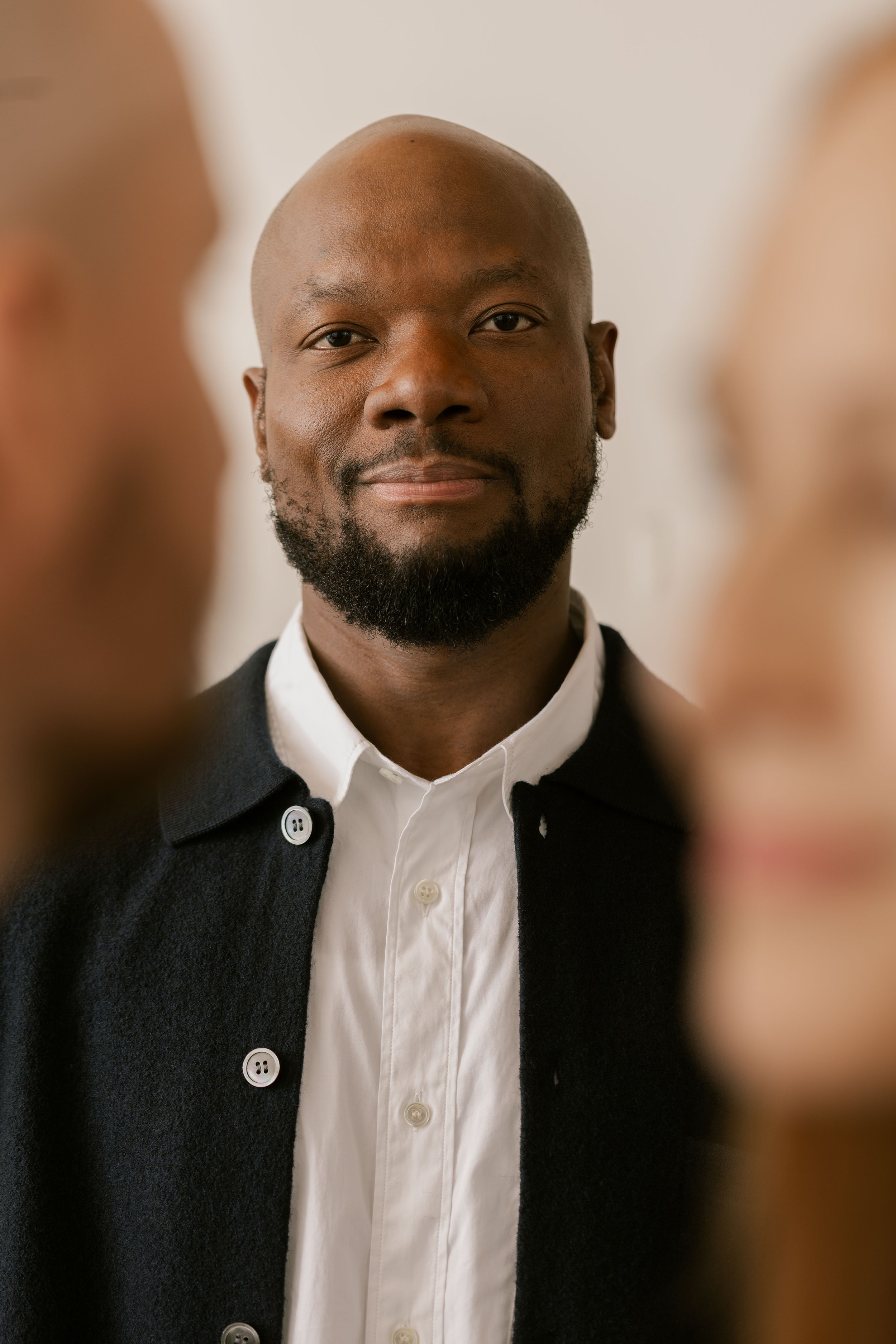 A man with a shaved head and beard looking directly at the camera, with two blurred figures in the foreground. Brand photography for banking.
