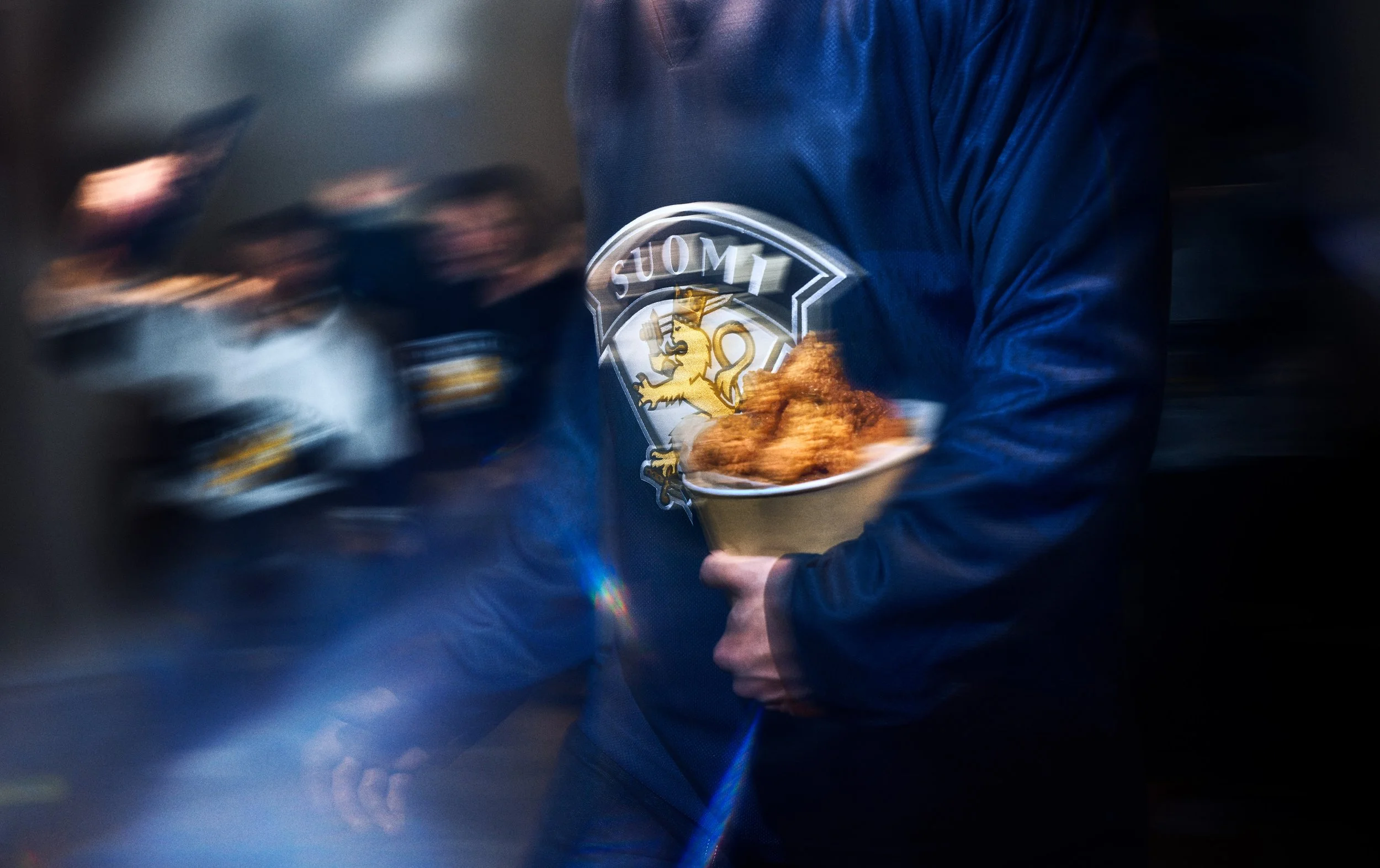 Personholding a bucket of fried chicken, watching a hockey came. Ad photo for hockey world championchips 2026.