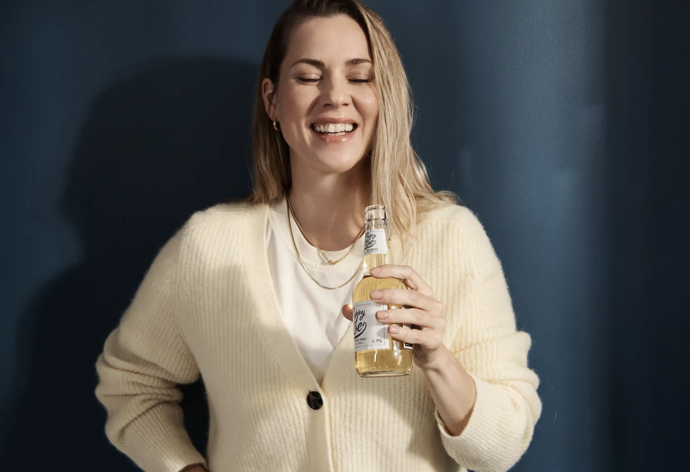 woman smiling with a drink on a blue backround. brand photography for hartwall