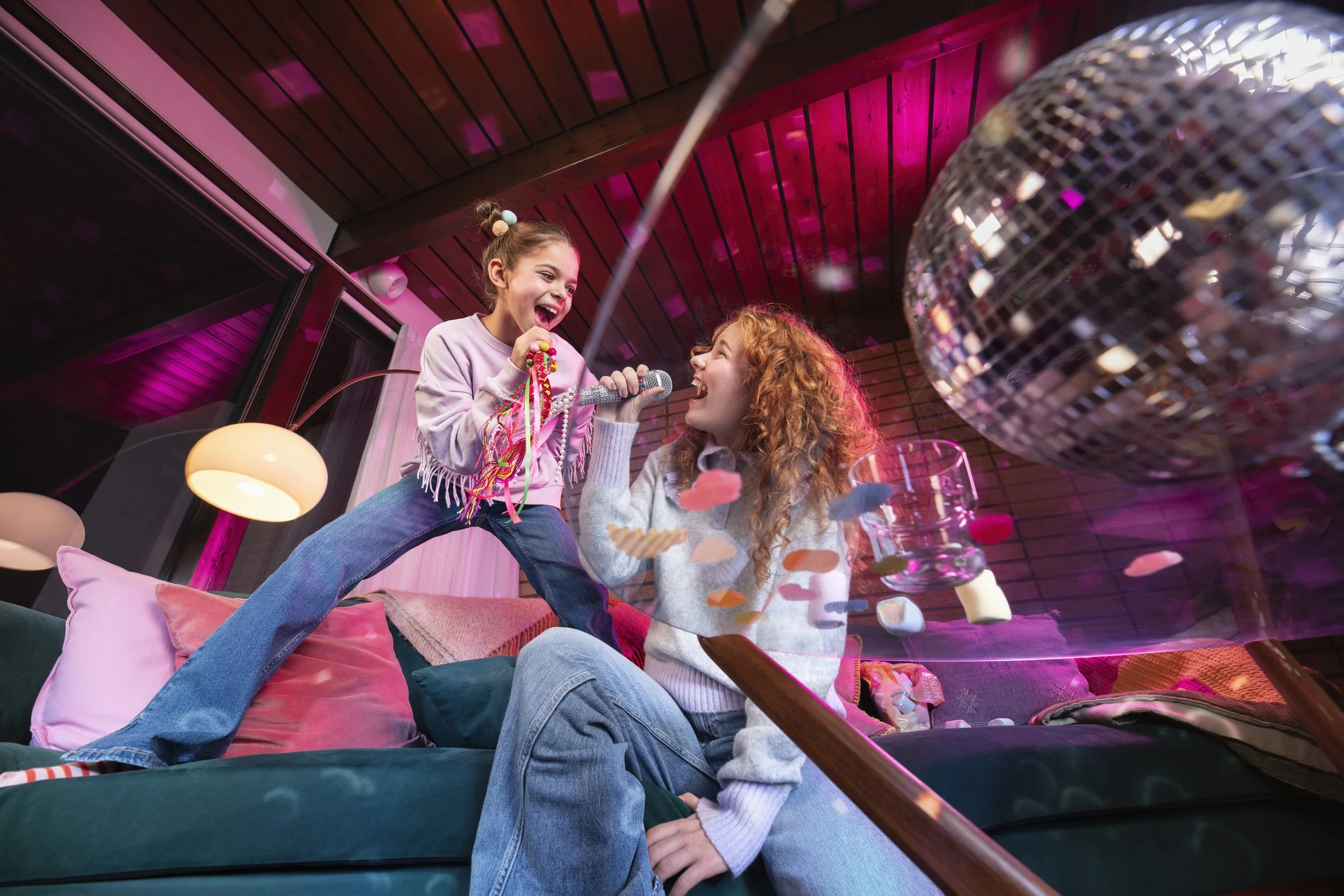 two girls singing karaoke on sofa. brand photography