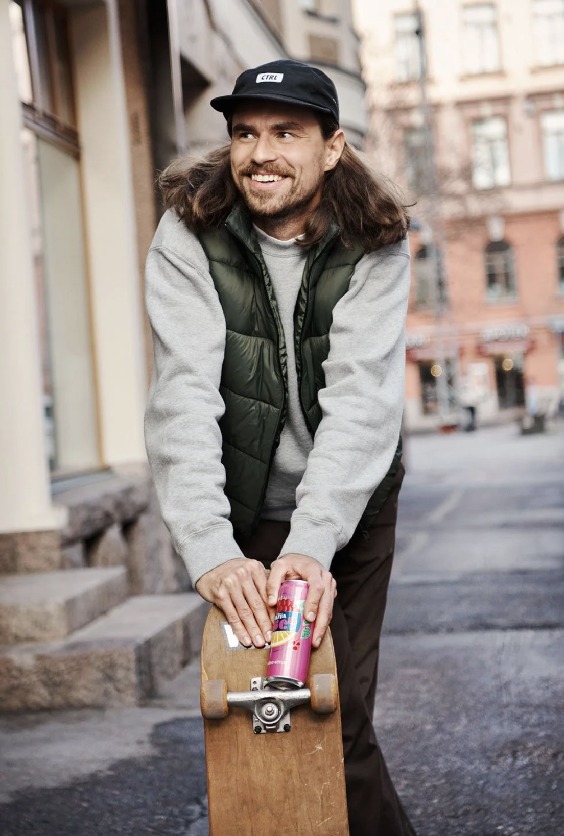man with skate board and soda on the street smiling. brand photography