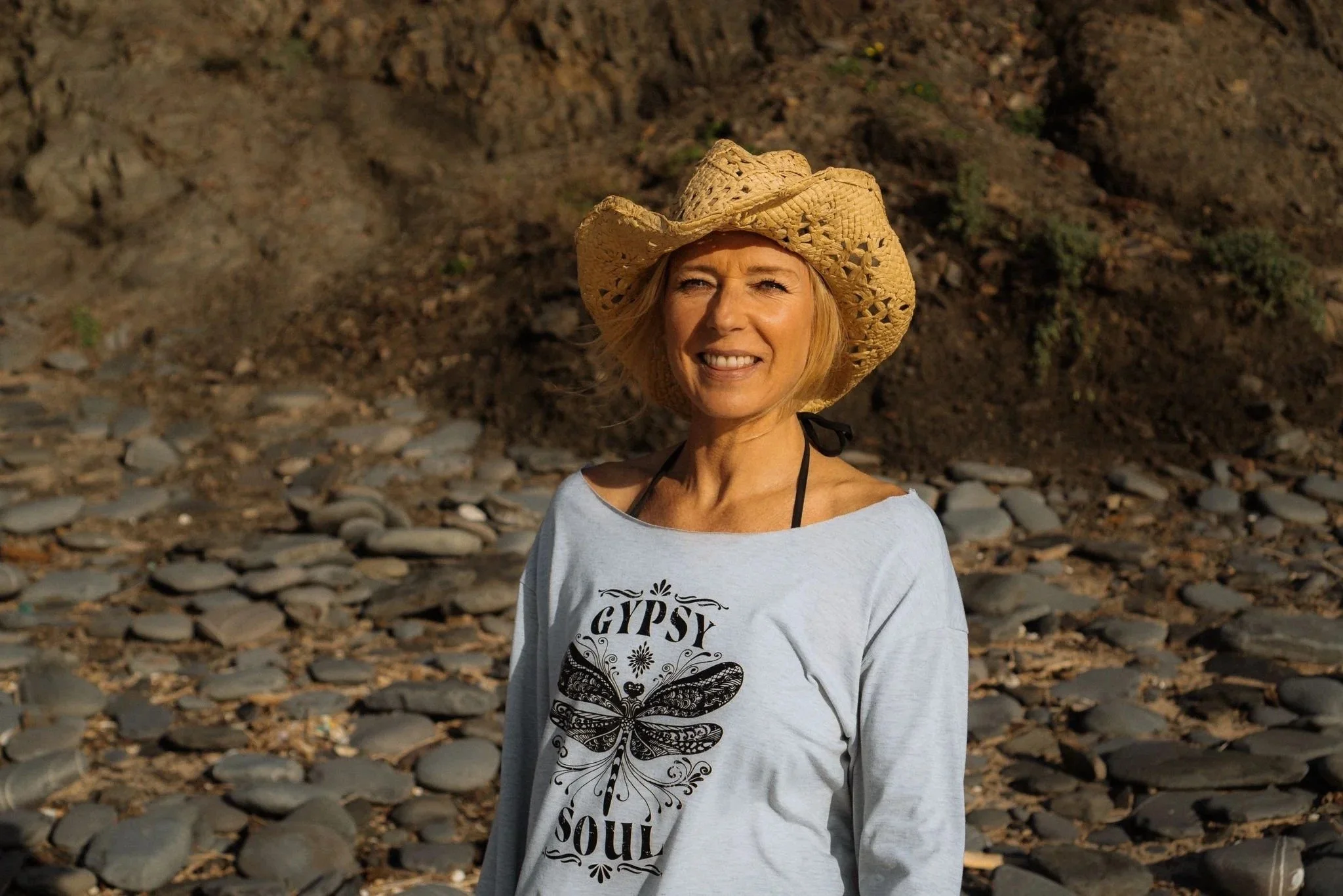 Kaja Dass Pavan in a straw hat, smiling in front of a rock on a beach in Portugal