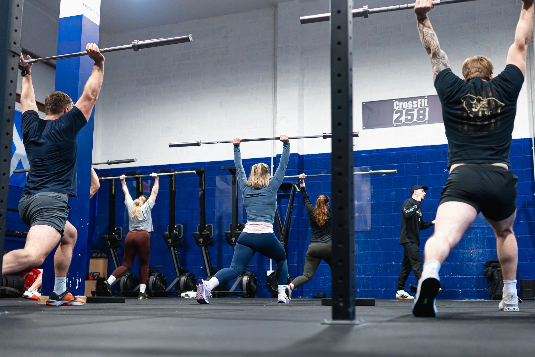 People participating in a CrossFit workout in a gym, lifting barbells overhead while wearing athletic clothing.
