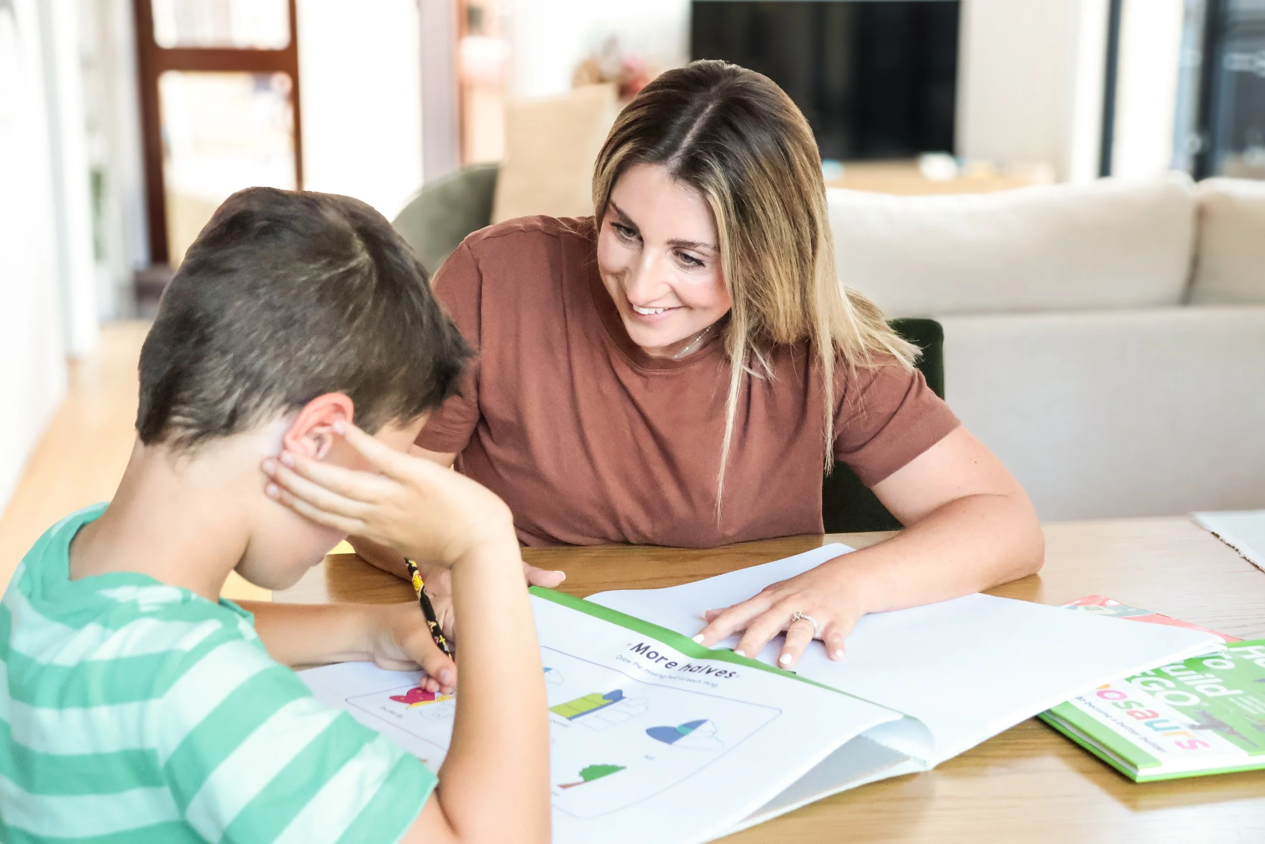 Rachael and a young boy sitting at a table working on a colorful activity sheet together in a bright, cozy room.