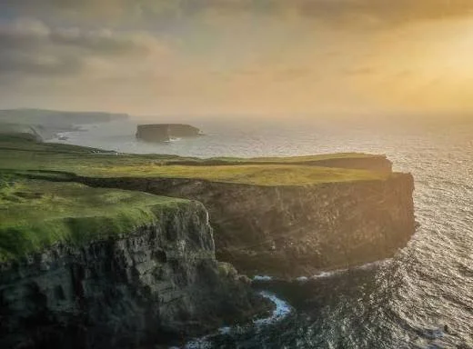 Cliffs overlooking the ocean at sunset with grassy tops and rugged edges.