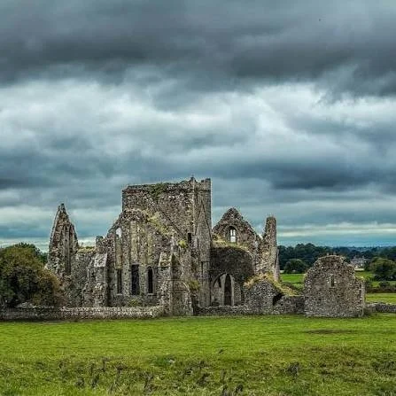 Ruins of an old stone castle on a grassy field under a cloudy sky.