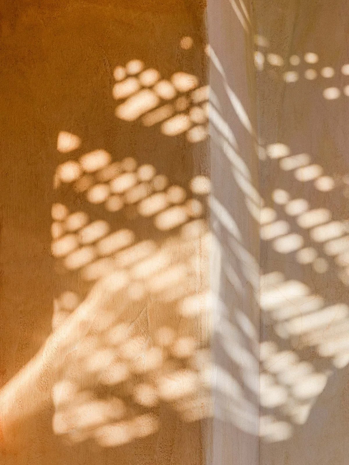 Close-up of a hand casting shadows of a pattern onto a brown wall, created by a textured surface with small openings.