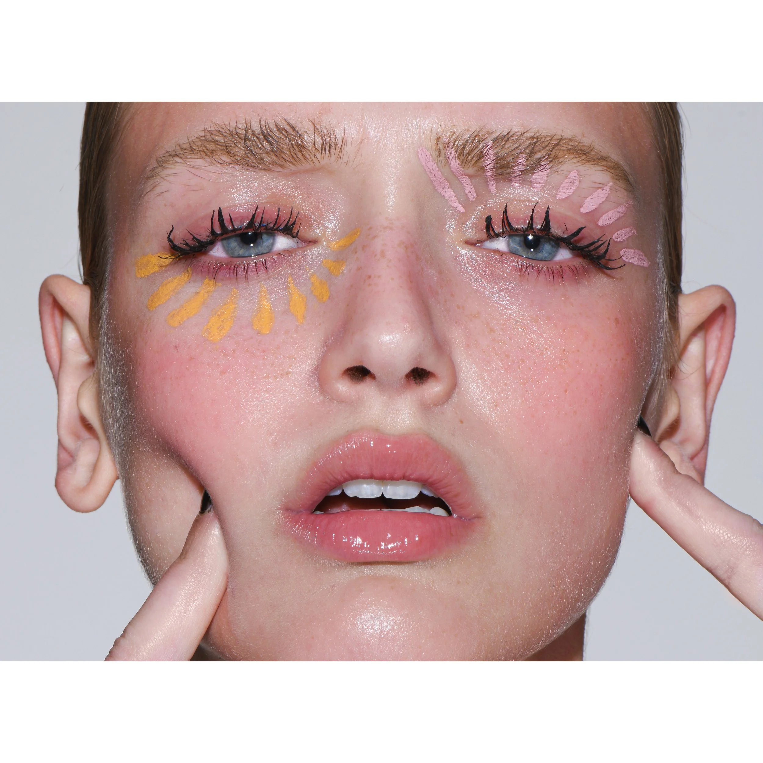 Nahaufnahme eines Gesichts, das mit bunten Farben und Muster geschminkt ist, einschließlich blauer Augen, pinken und gelben Mustern um die Augen und Lippen