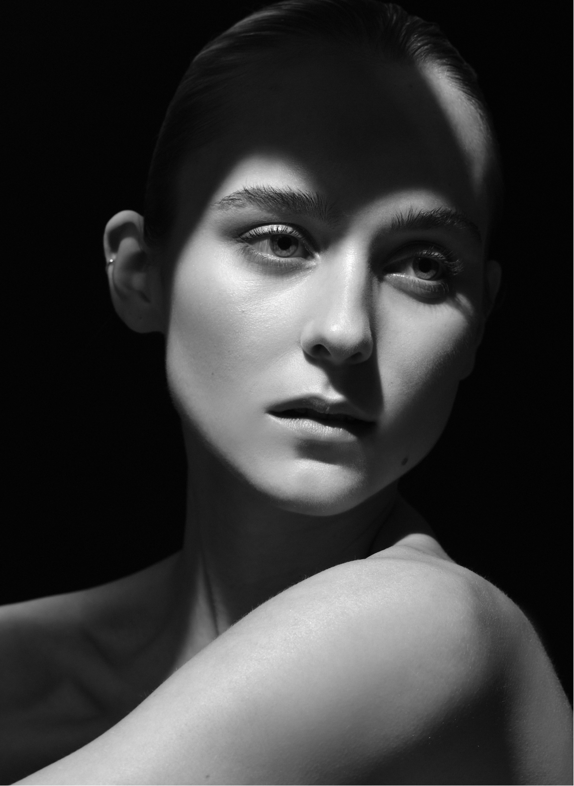 Schwarzweißfoto eines jungen Frauengesichts mit direktem Blick, teilweise im Schatten, mit glatter Haut und kurzen Haaren.