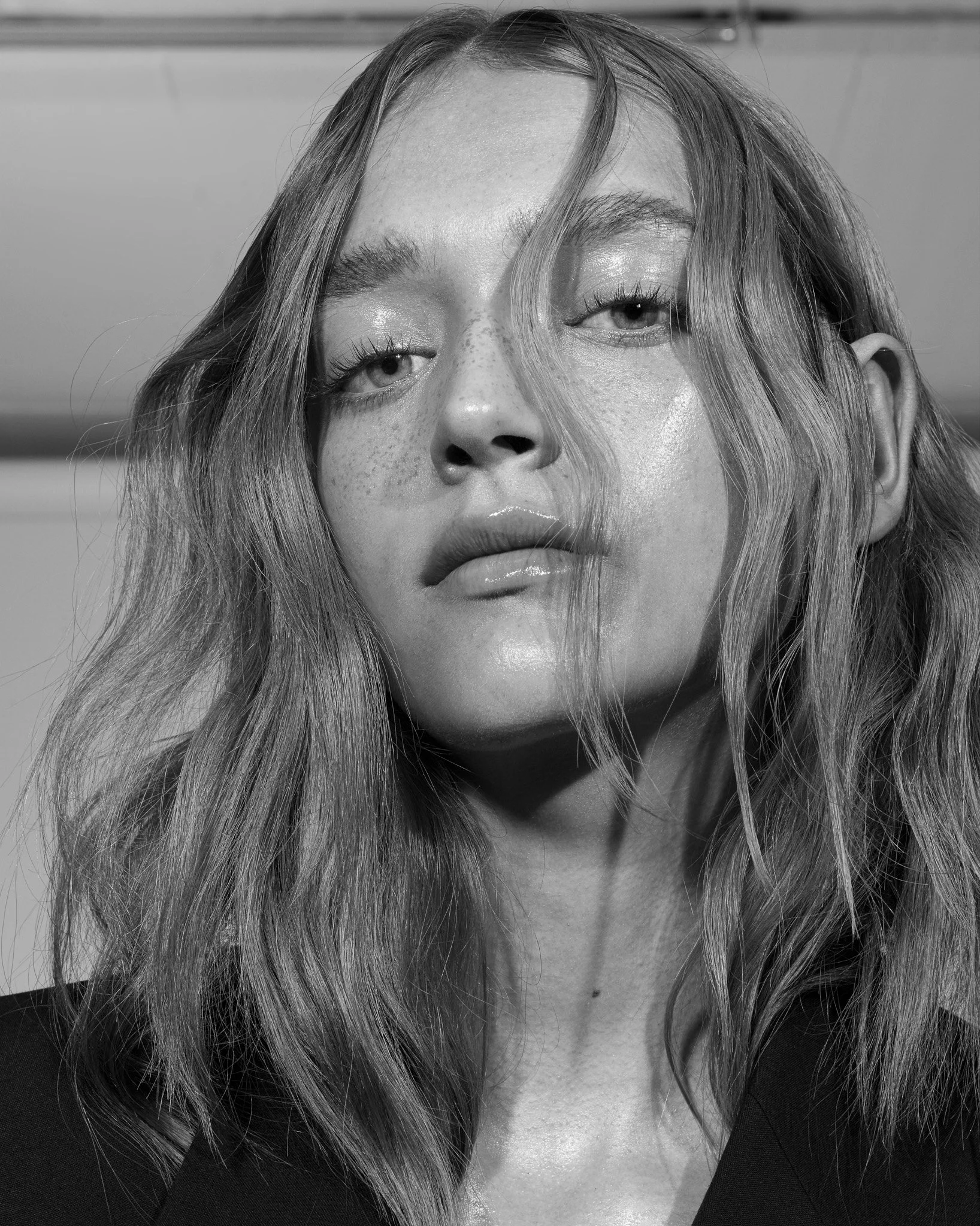Schwarz-Weiß-Fotografie eines Frauengesichts mit freckled Haut, lockigem Haar, halb geschlossenen Augen, glänzenden Lippen und schwarzer Kleidung.