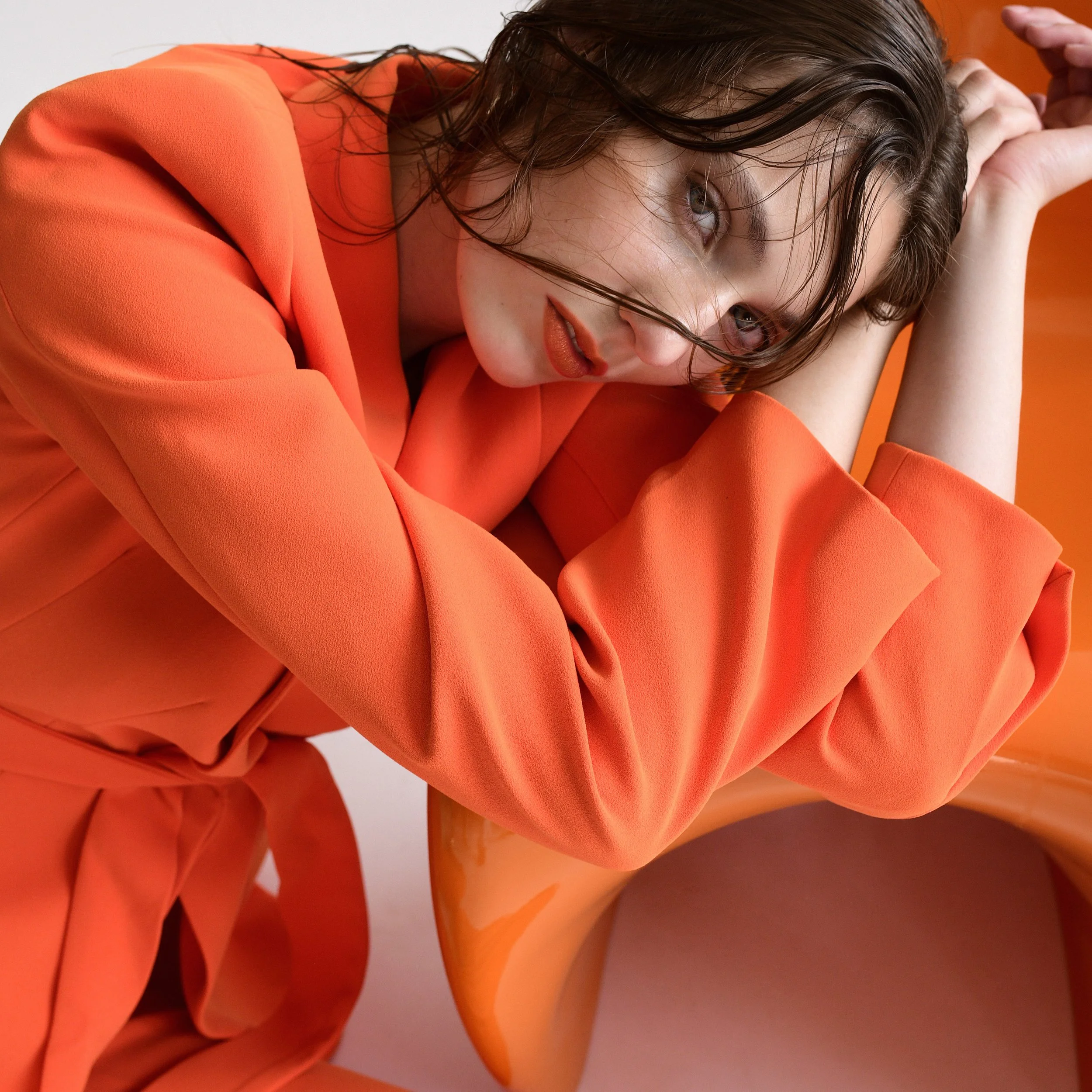Nahaufnahme einer jungen Frau mit nassen braunen Haaren, die ein orangefarbenes Outfit trägt und eine nachdenkliche Pose einnimmt.