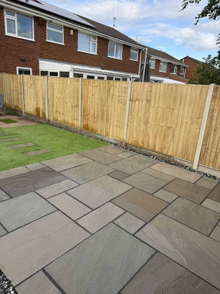Backyard with a wooden fence, grass area, concrete patio, and brick houses in the background.