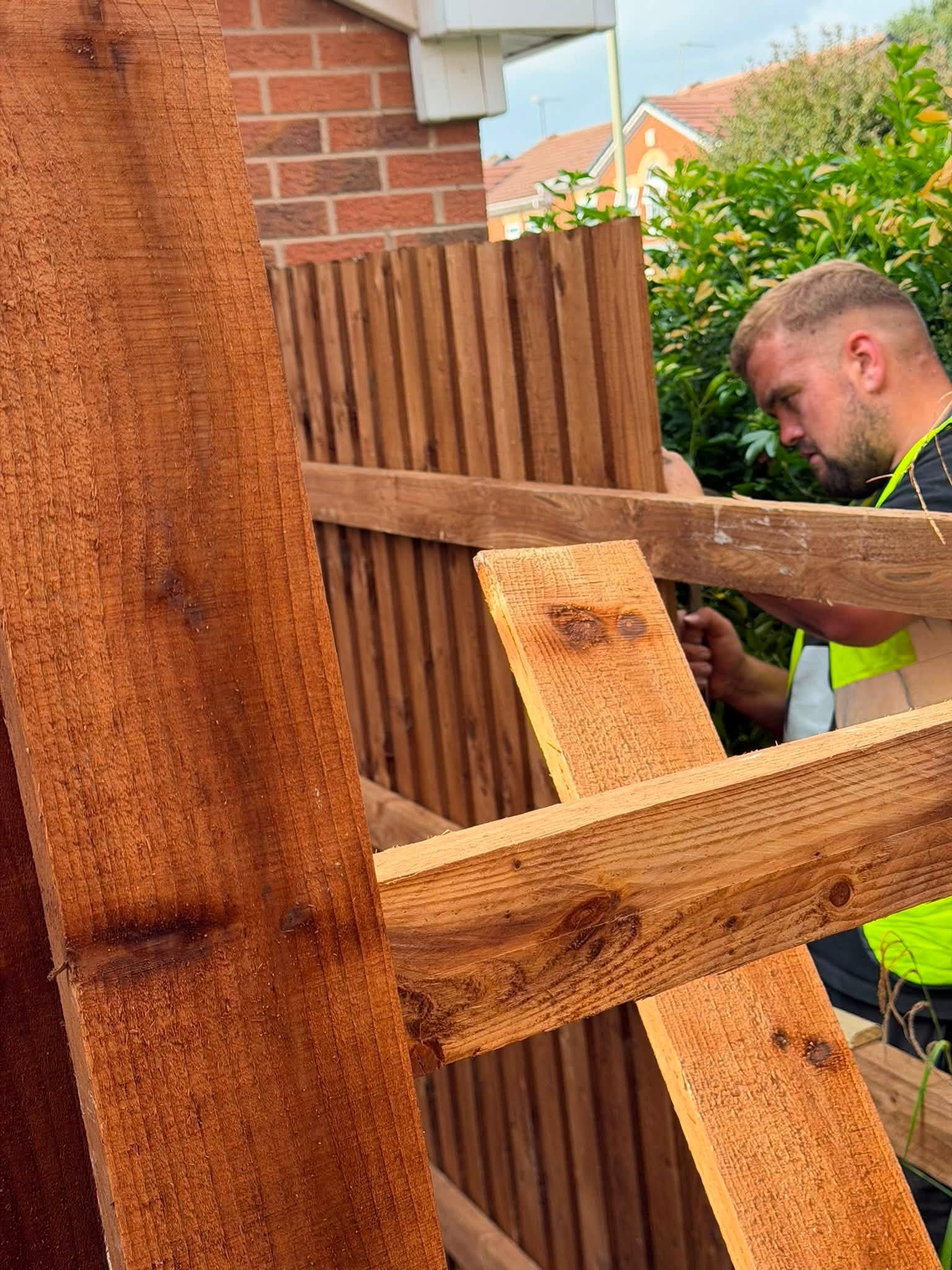 A man working on a wooden fence outdoors in a residential neighborhood.
