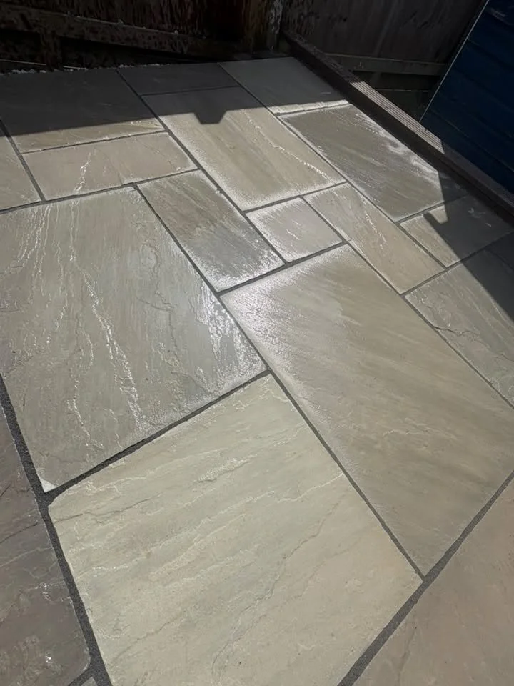 Close-up of a newly installed outdoor stone patio with beige and light gray textured tiles, partially shaded.