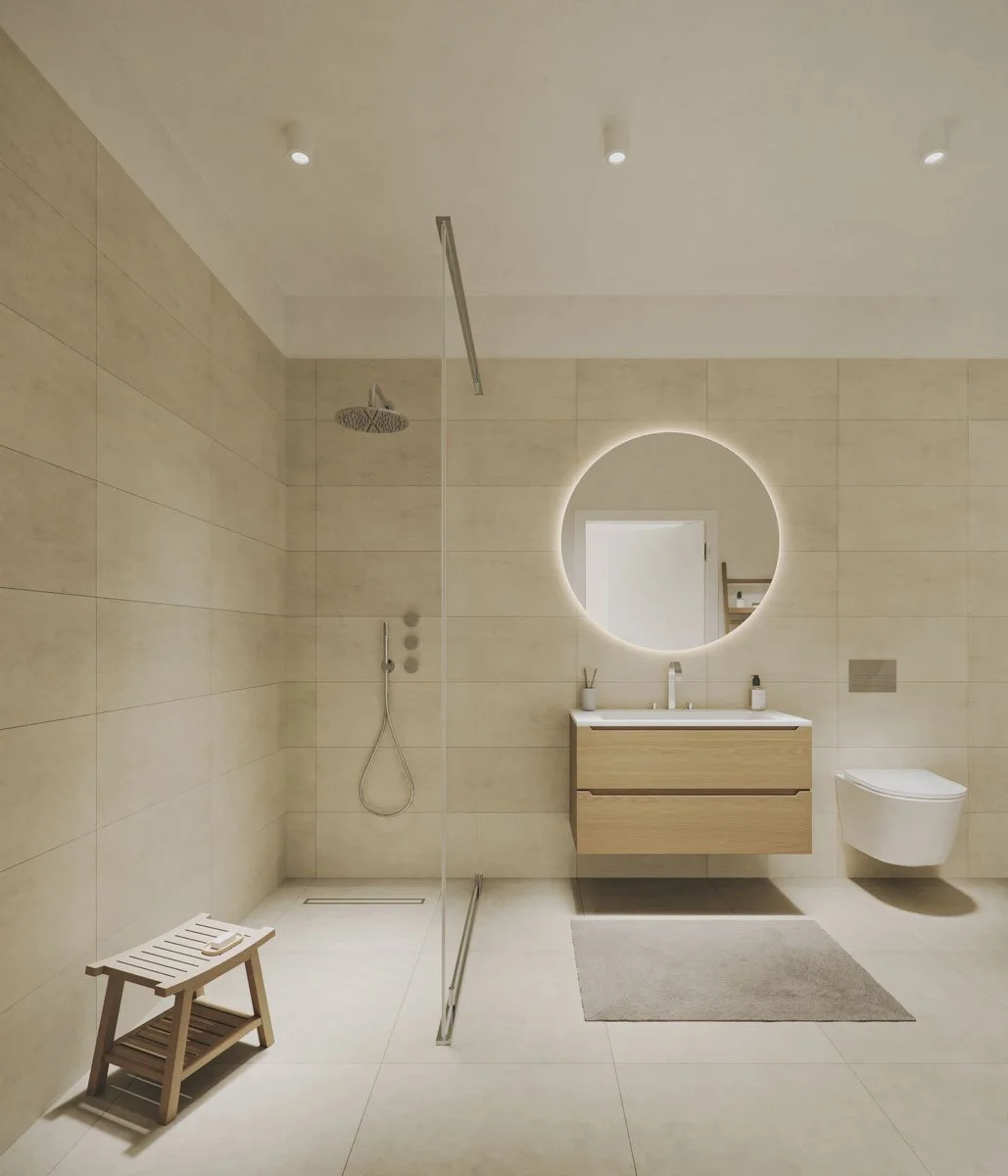 Bagno moderno con pareti in beige, specchio rotondo con retroilluminazione, lavabo in legno e ceramica, vasca doccia aperta senza porte, soffitto con faretti, tappetino grigio, sedile in legno, uno spray per la doccia e altri piccoli oggetti di arred