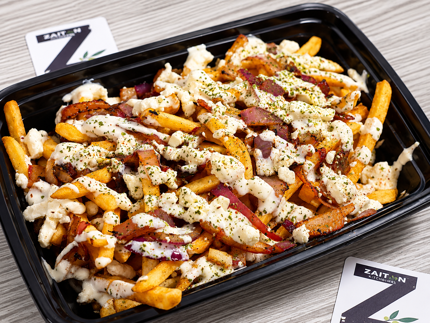 Container of loaded fries topped with various cheeses, bacon bits, and herbs, on a wooden surface.