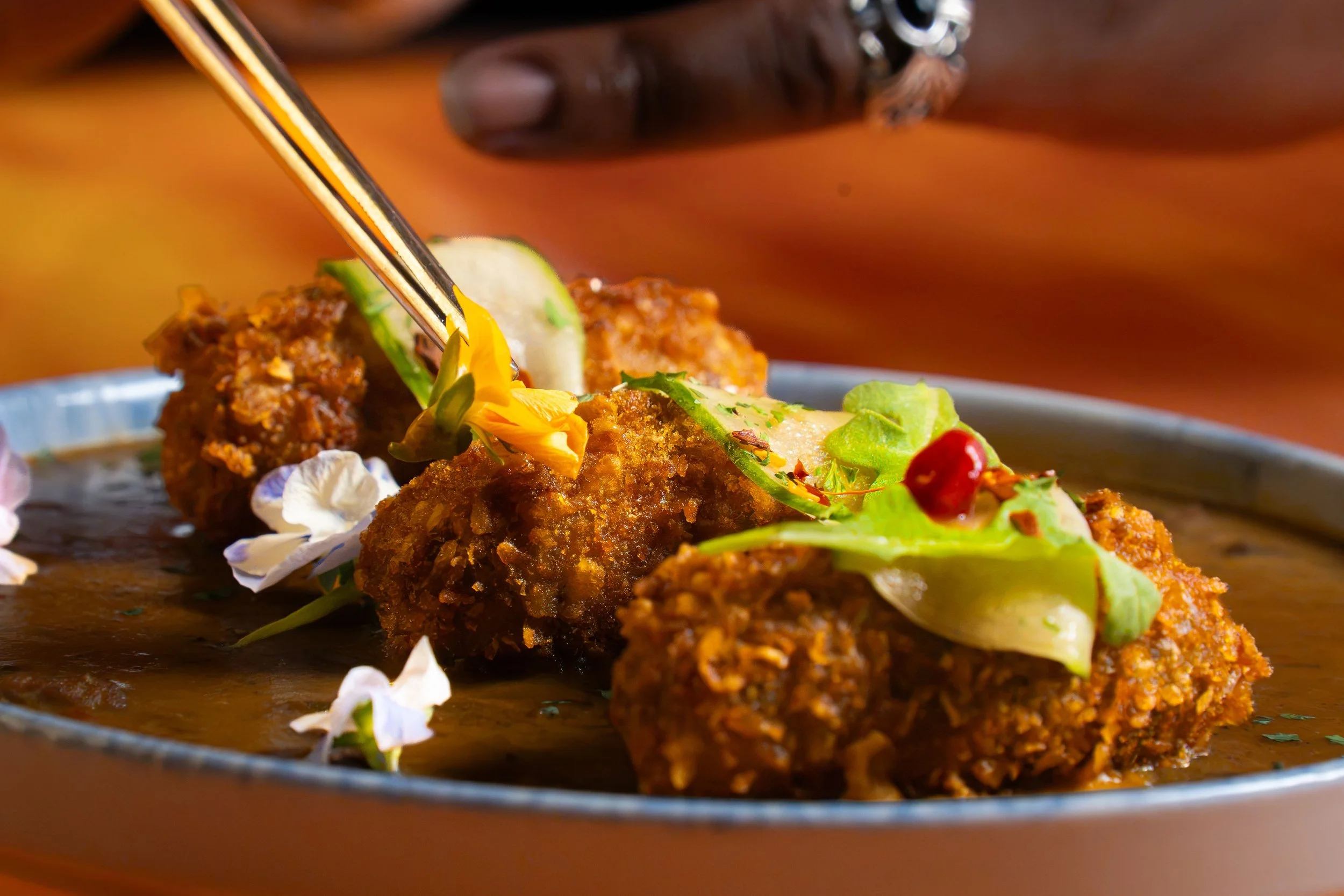 Close-up of fried food balls garnished with fresh greens, edible flowers, and a red berry on a plate.