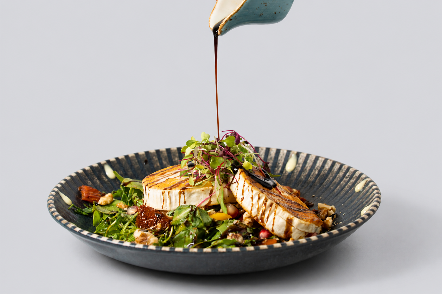 Grilled chicken breast atop a bed of mixed greens and microgreens, drizzled with balsamic glaze and dressing, served on a blue patterned plate.