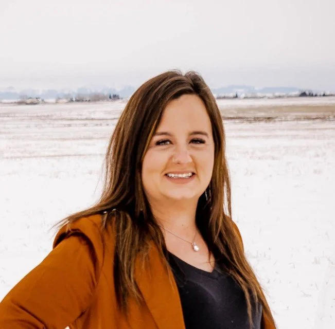 A woman with long brown hair smiling outdoors in a snowy landscape.