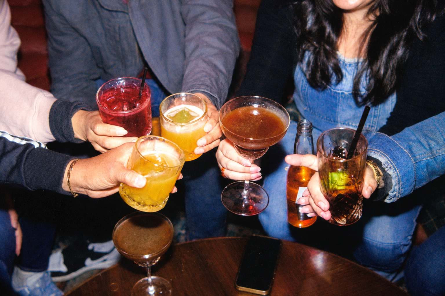 Group of people holding colorful cocktails and drinks in a bar or restaurant setting.